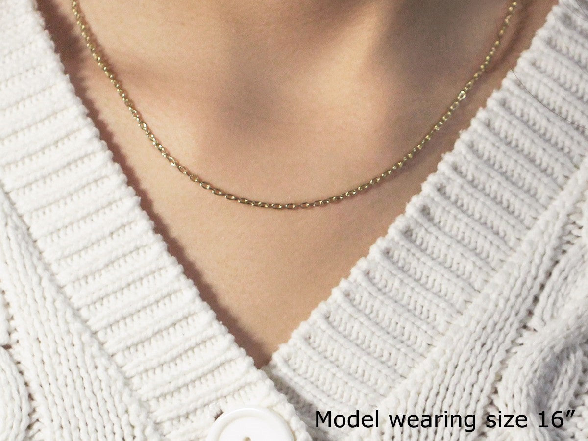 A 14k yellow gold cable chain is worn around a person's neck over a white sweater.