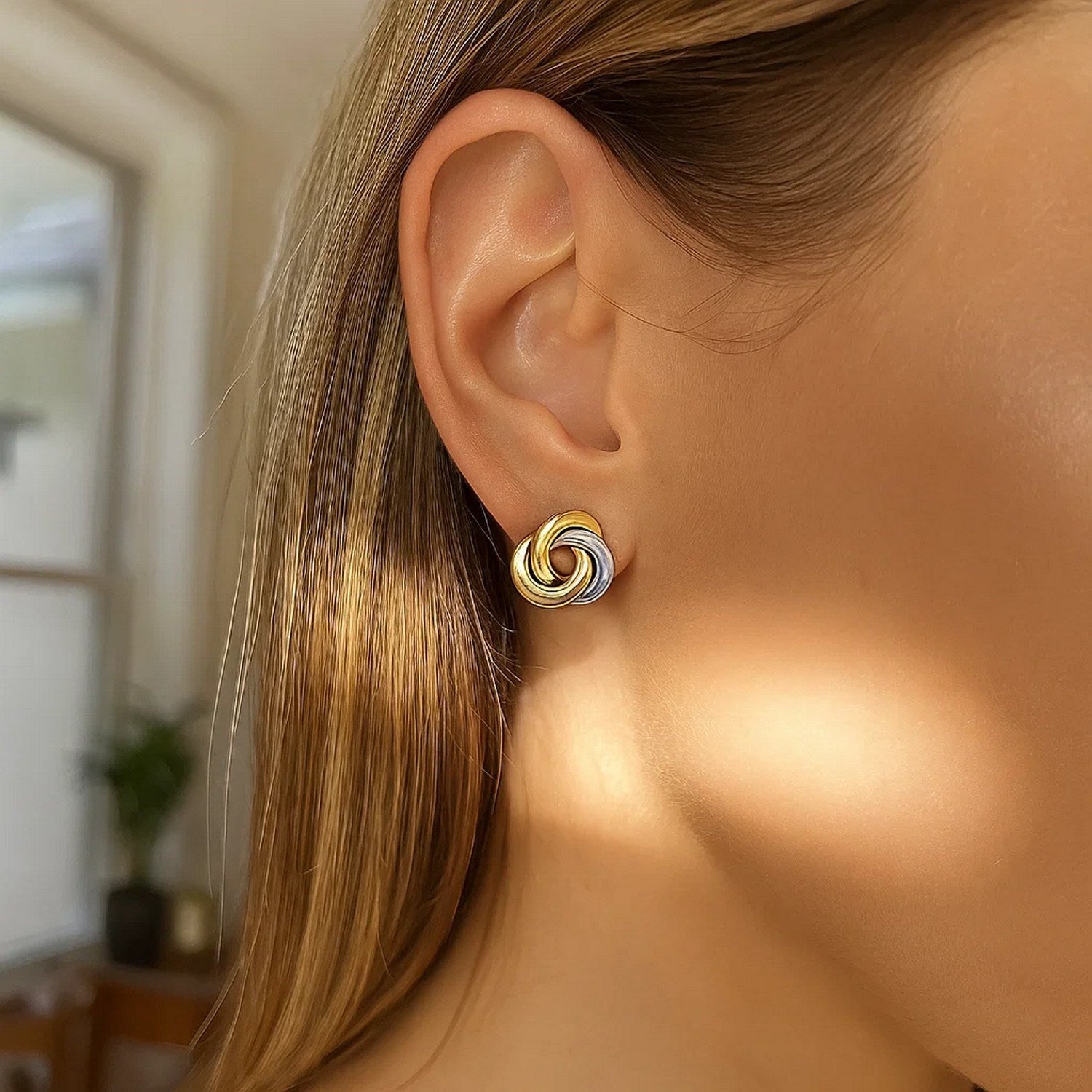 14k two-tone gold shiny intertwined open circle earrings on an ear.