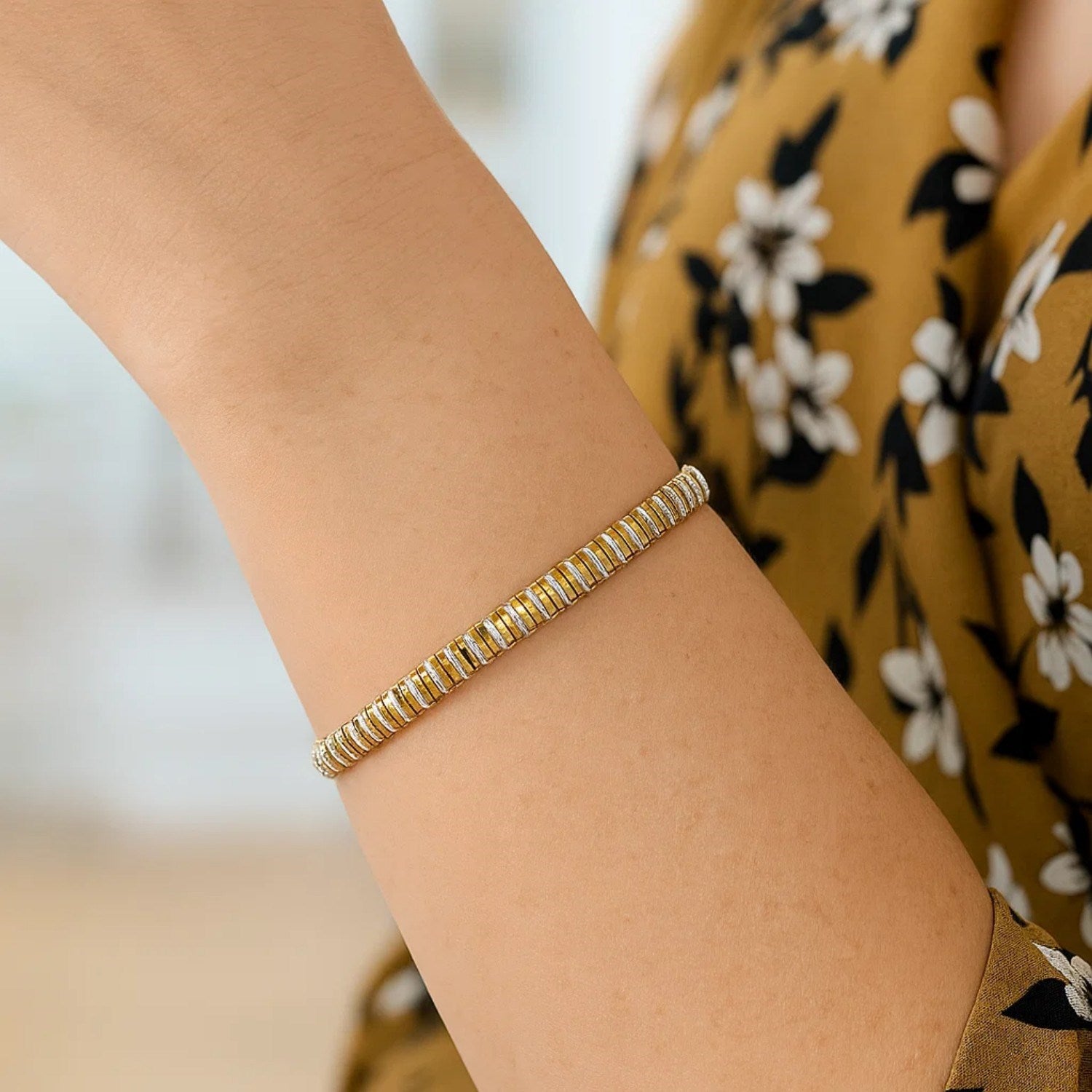 A two-tone gold bracelet with alternating gold and silver segments on a woman's arm.