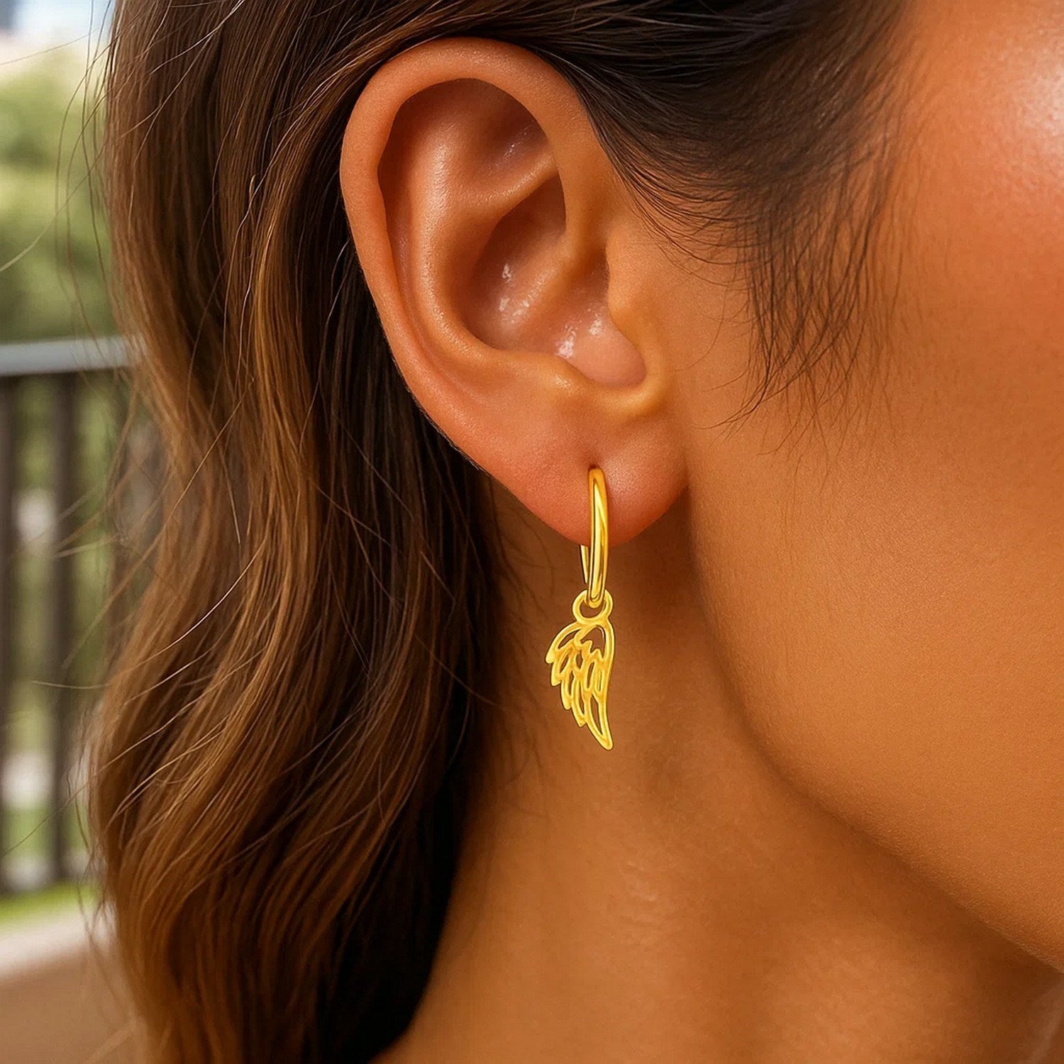 14K yellow gold hoop earrings with angel wings on a person's ear.