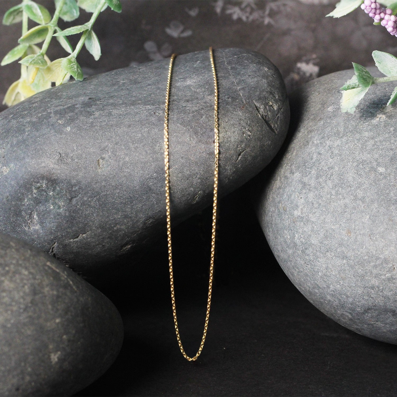 An 18k yellow gold round cable link chain rests on dark grey stones.