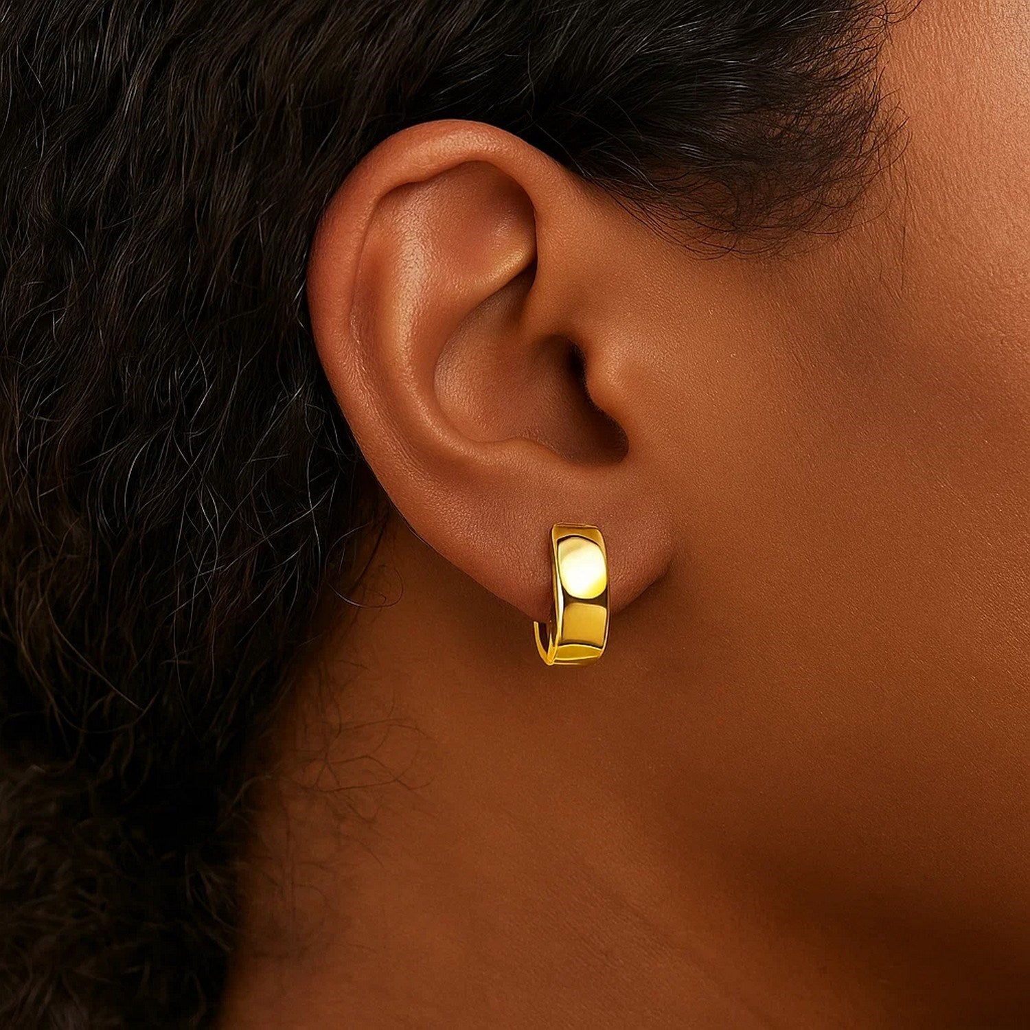 A single 10k yellow gold snuggable hoop earring is worn on an ear.