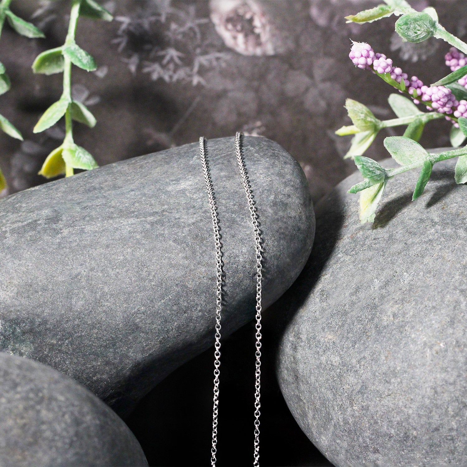 A 14k white gold round cable link chain, 1.10 mm wide, rests on gray stones.