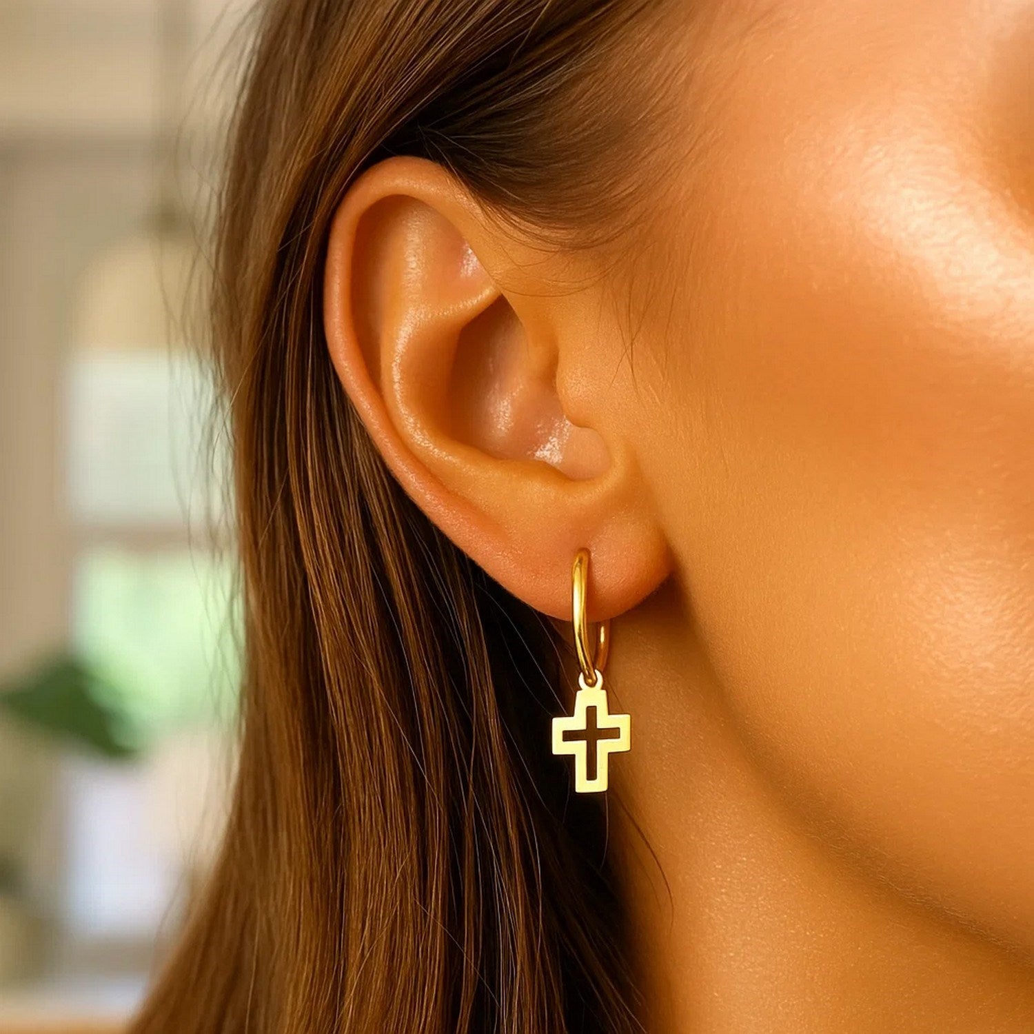 A woman wears a single 14K yellow gold hoop earring with a cross charm.
