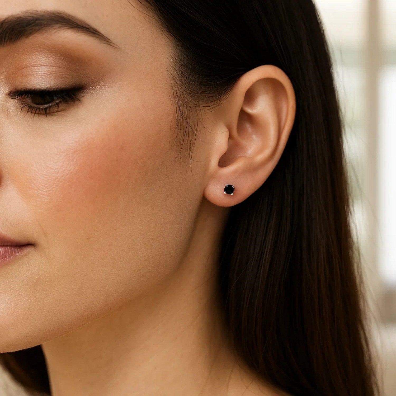 A woman wears a single 14k white gold black 3mm faceted cubic zirconia stud earring.