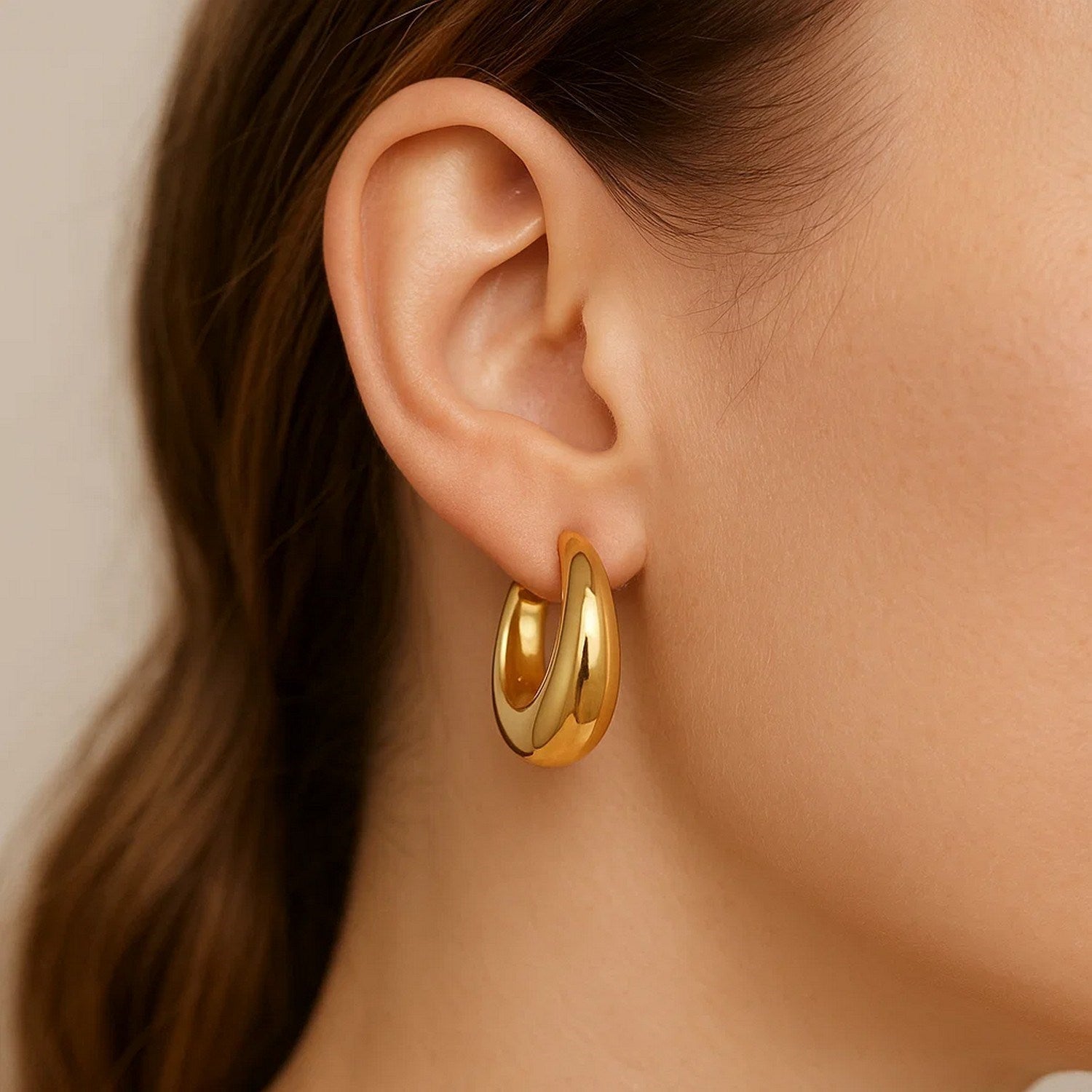 Medium tapered hoop earrings in 14K yellow gold on a model's ear.