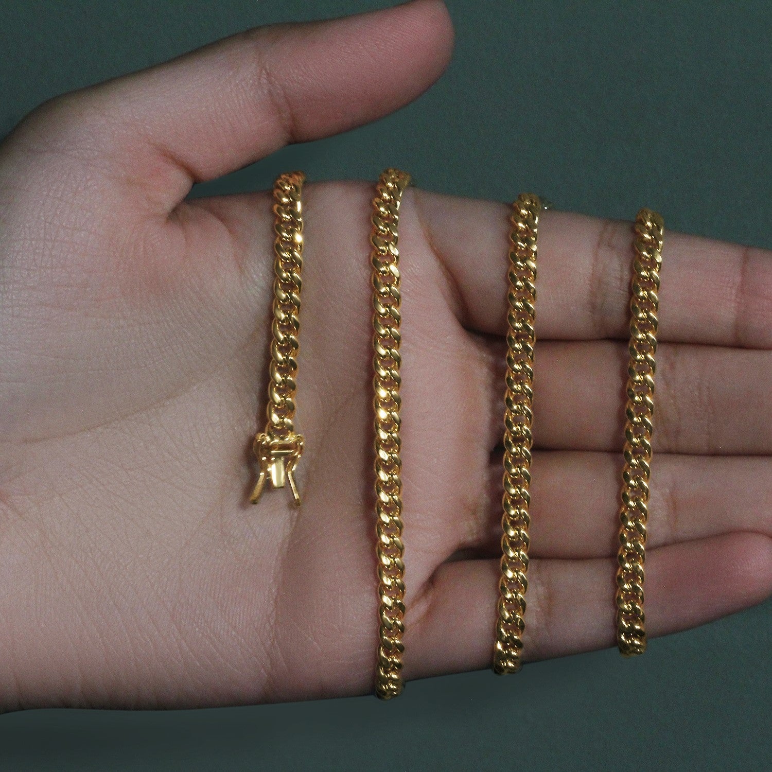 A 14k yellow gold semi-solid Miami Cuban chain with a box clasp, held in a hand.
