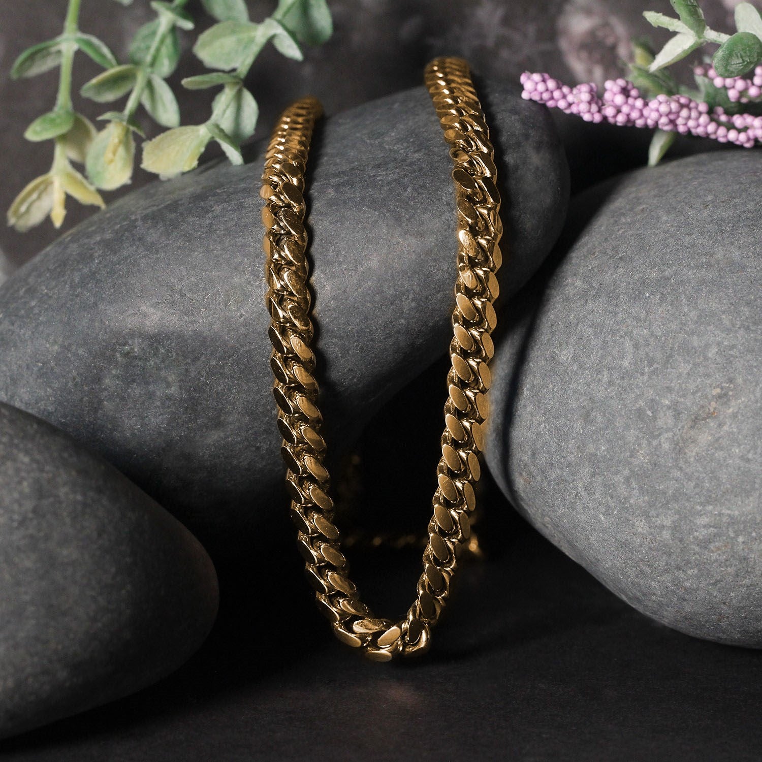 A 14k yellow gold classic Miami Cuban solid chain rests on dark grey rocks.
