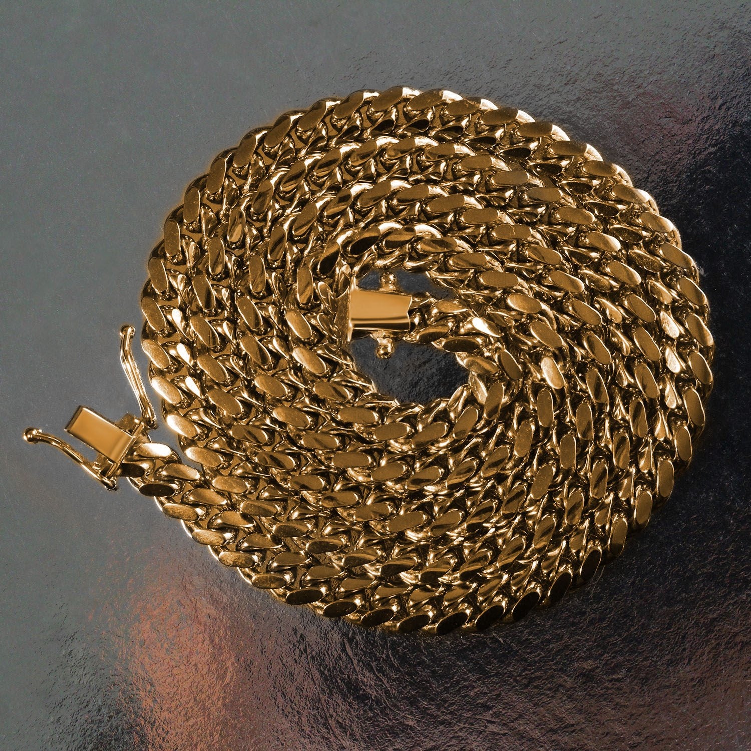 A 14k yellow gold classic Miami Cuban solid chain, 6.10 mm wide, coiled on a reflective surface.