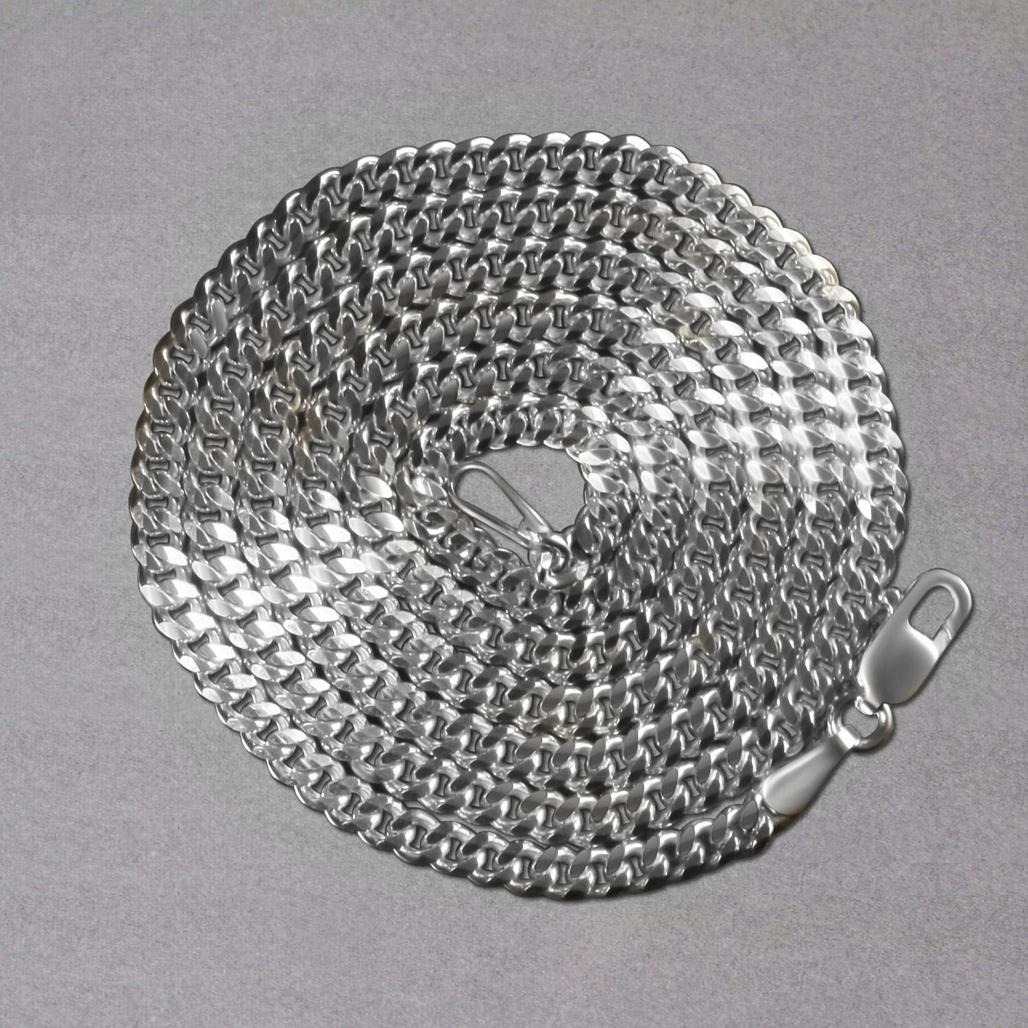 A 14K white gold gourmette chain with a lobster clasp, coiled on a gray surface.