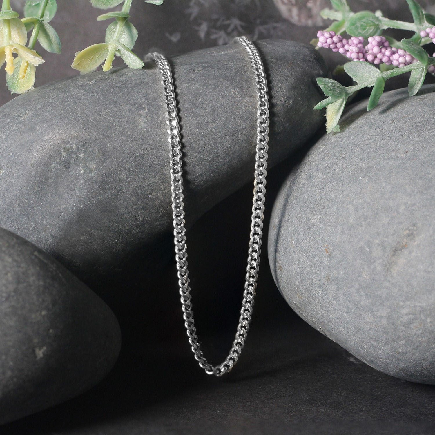 A 14K white gold gourmette chain is draped over smooth grey stones.