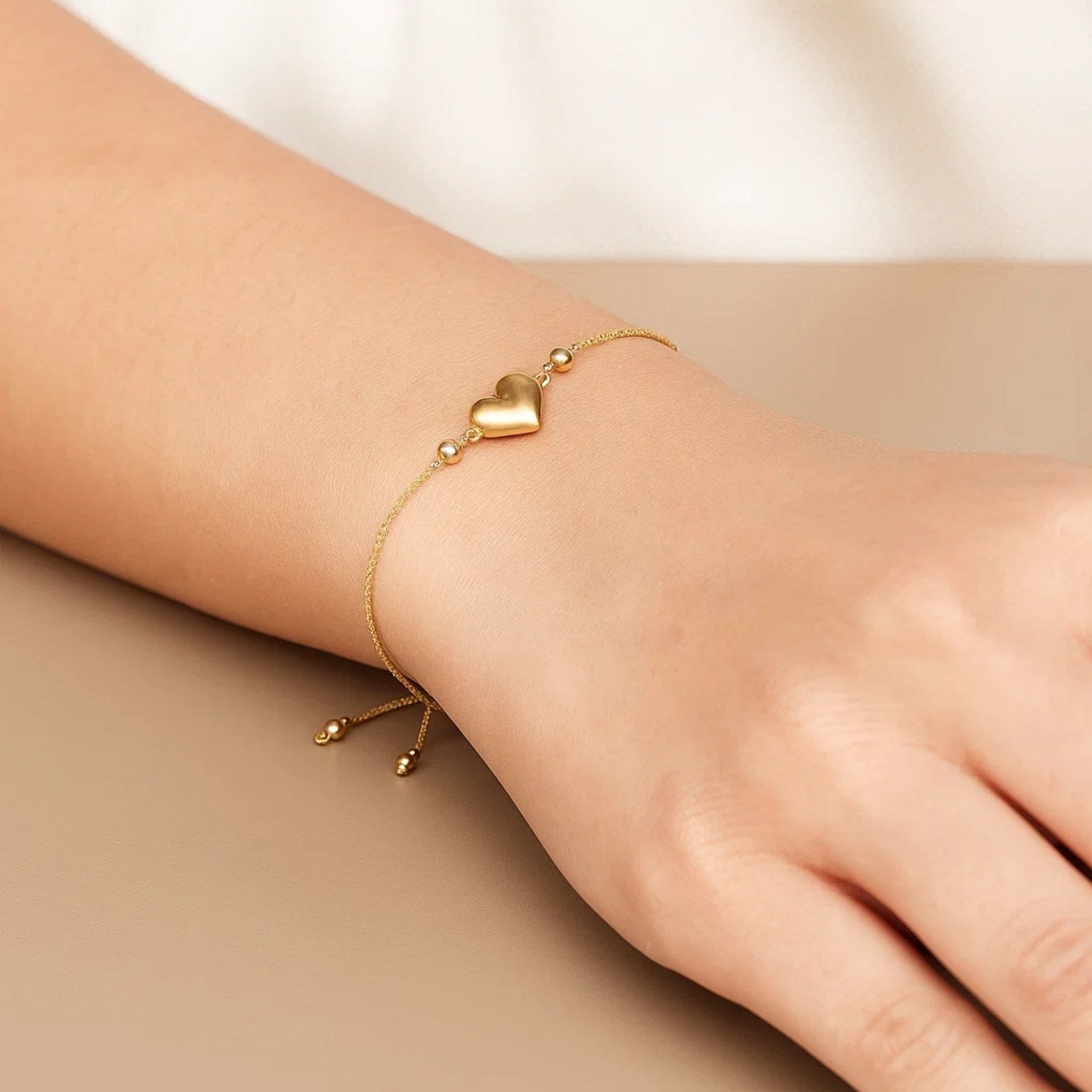 An adjustable 14K yellow gold bracelet with a puffed heart charm and two beads.