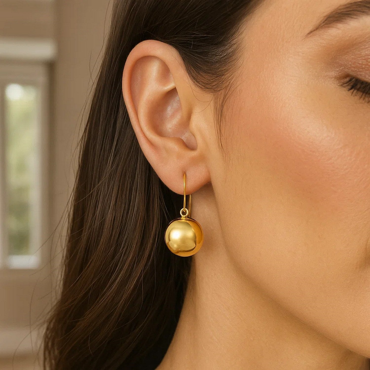 14k yellow gold puffed circle drop earrings on a woman's ear.