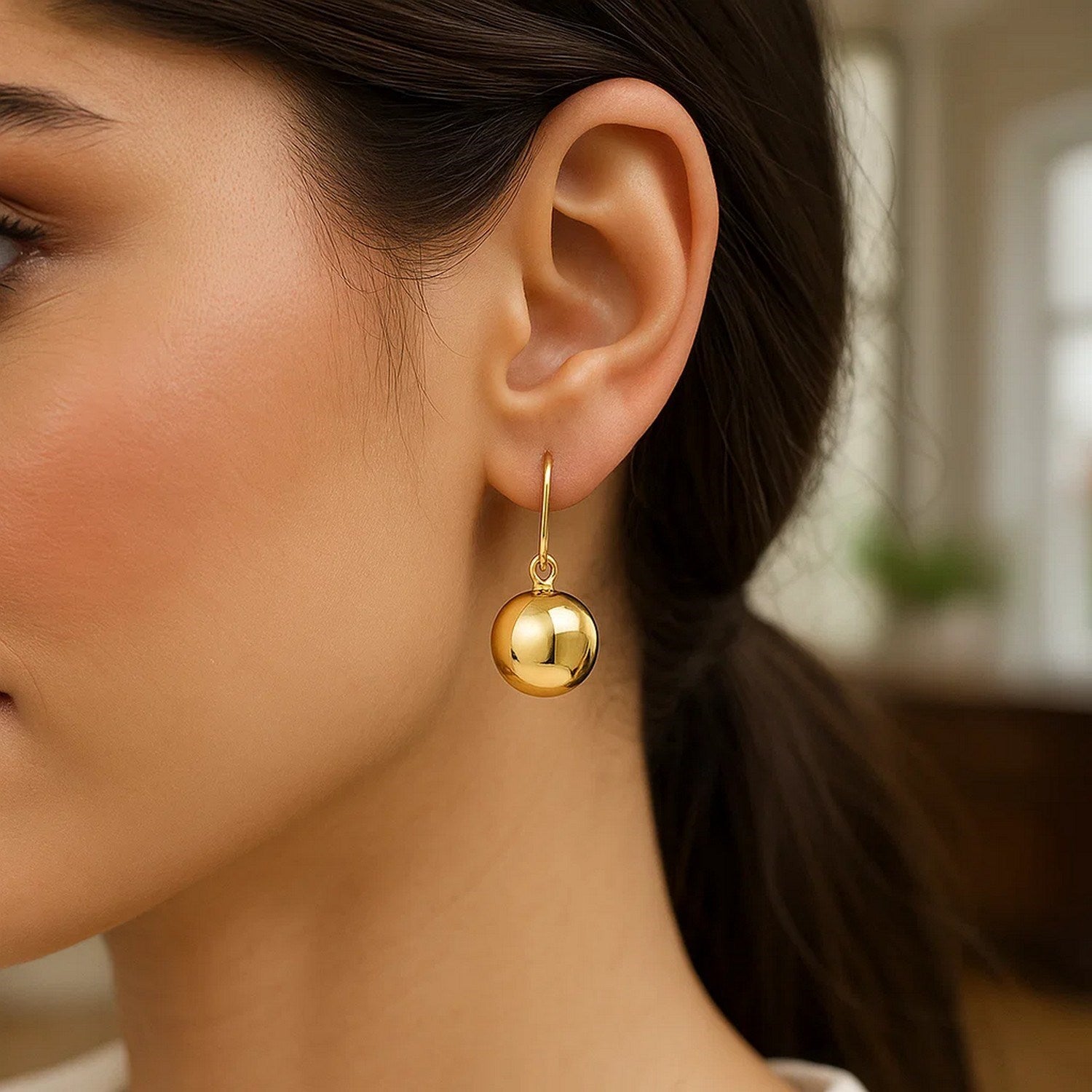 14k yellow gold puffed circle drop earrings on a woman's ear.