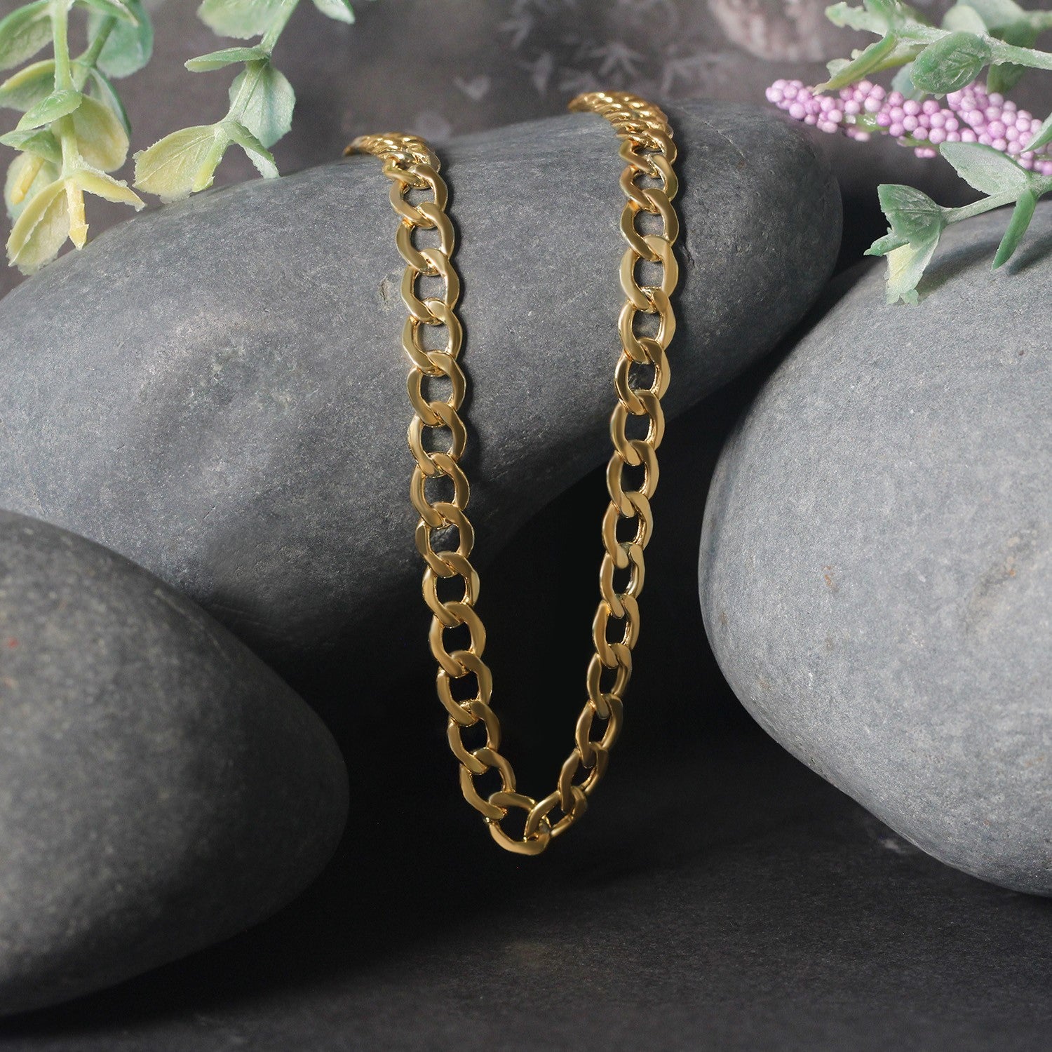 10k yellow gold curb chain on dark gray rocks with green and purple foliage.