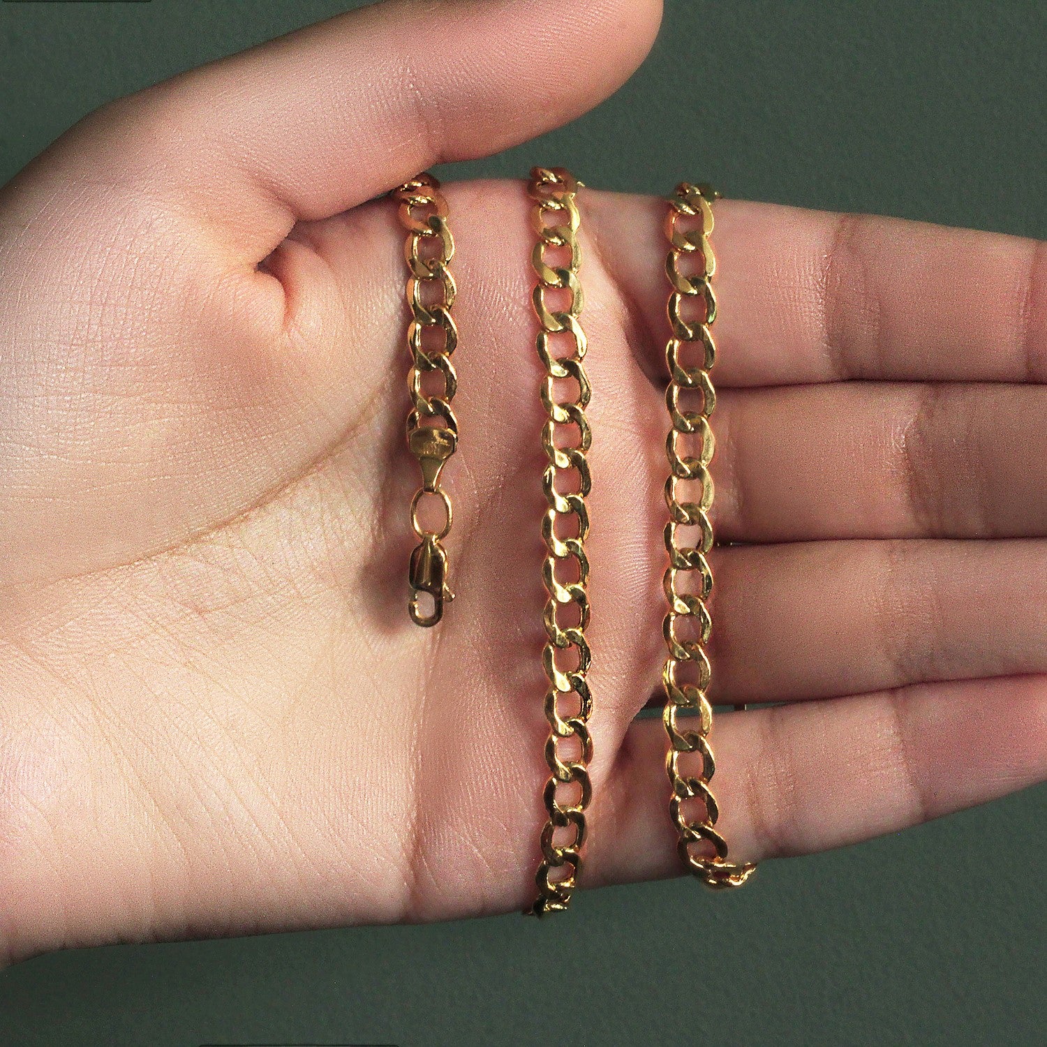 A 10k yellow gold curb chain with a lobster clasp is held open on a hand.