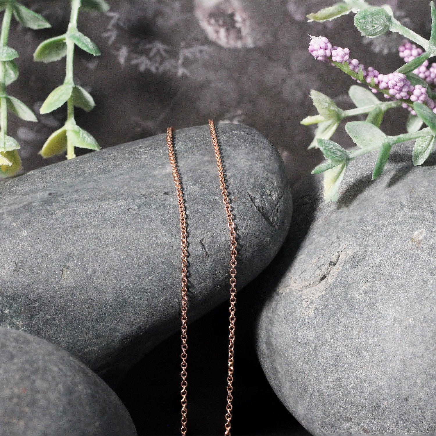 14k rose gold round cable link chain (1.25 mm) draped over grey stones.