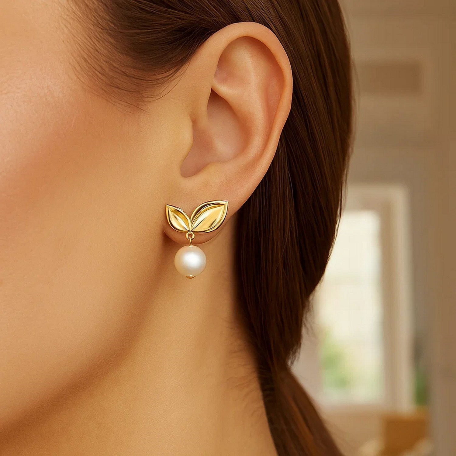 A woman wears a gold cherry leaf earring with a pearl drop.