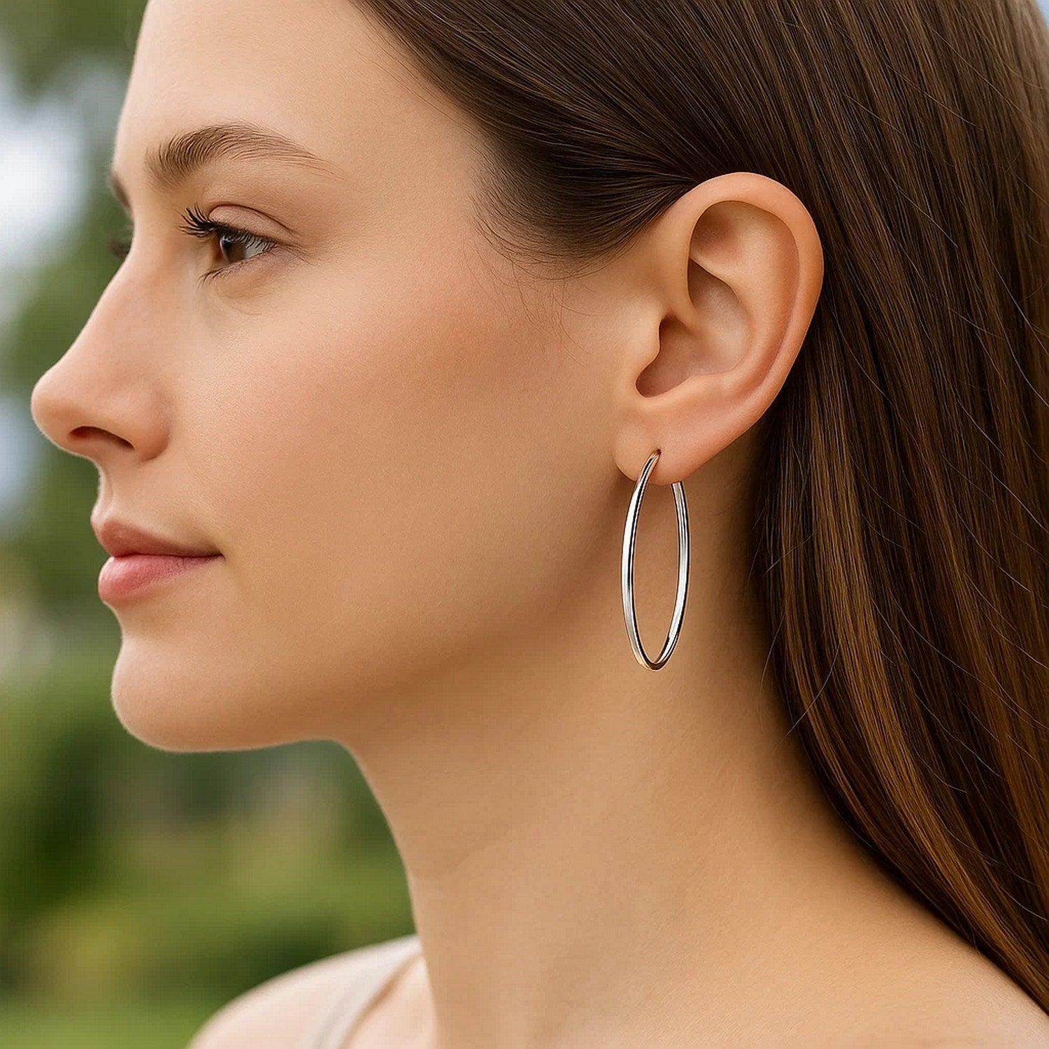 A woman wears 14k white gold slim oval hoop earrings.