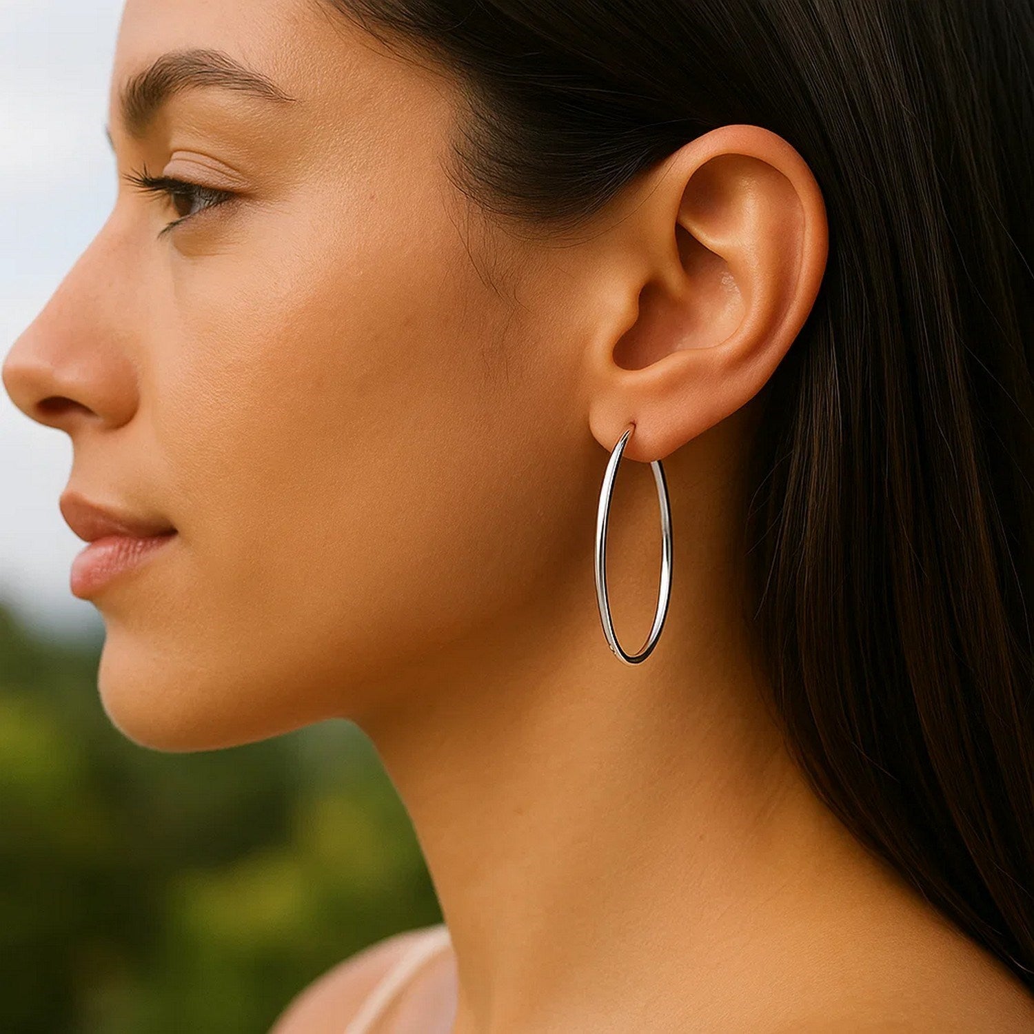 14k white gold slim oval shape hoop earrings on a woman's ear.
