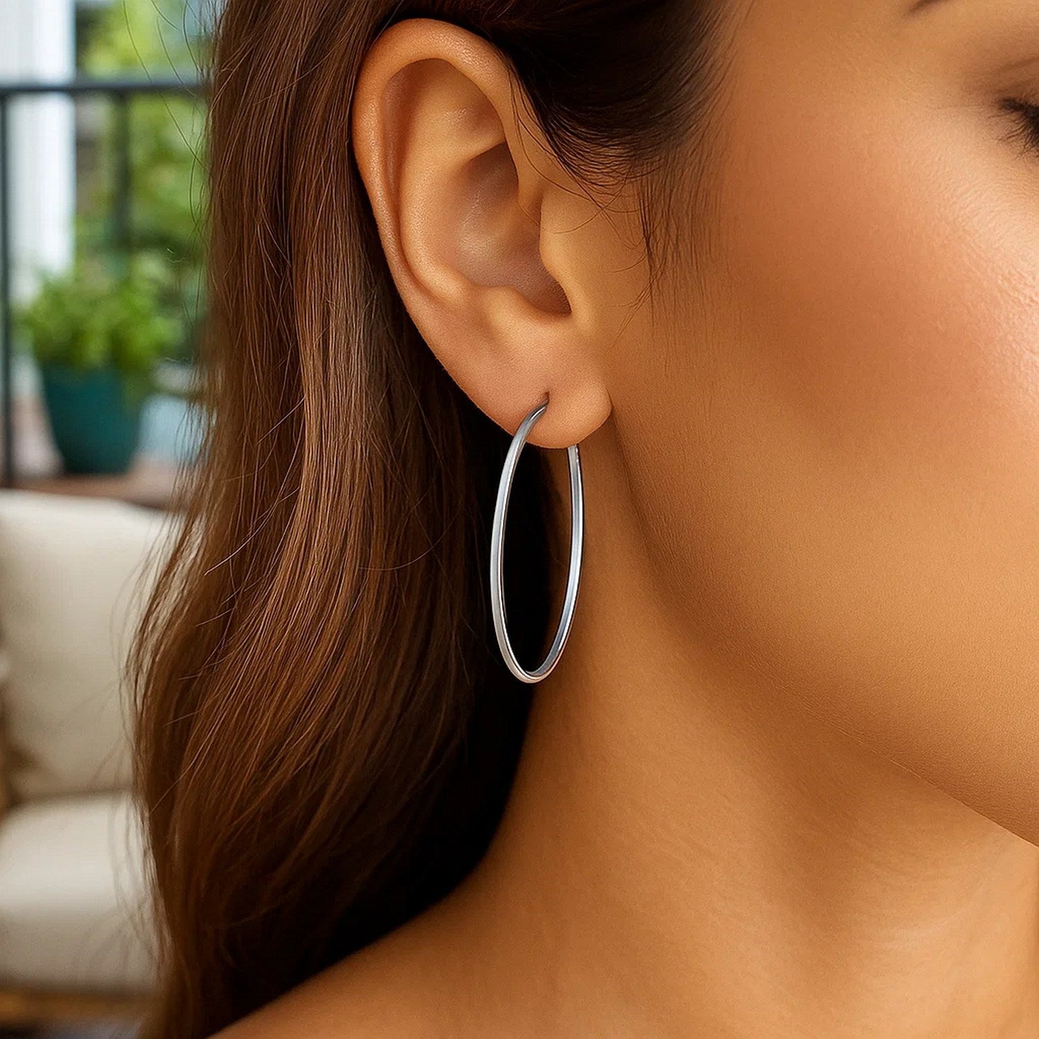 A woman wears 14k white gold slim oval hoop earrings.