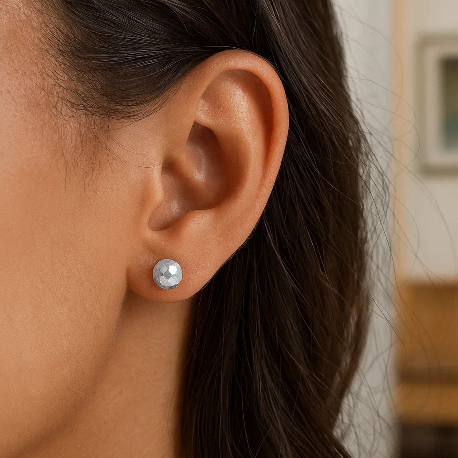 A woman wears a single 14k white gold faceted ball earring.