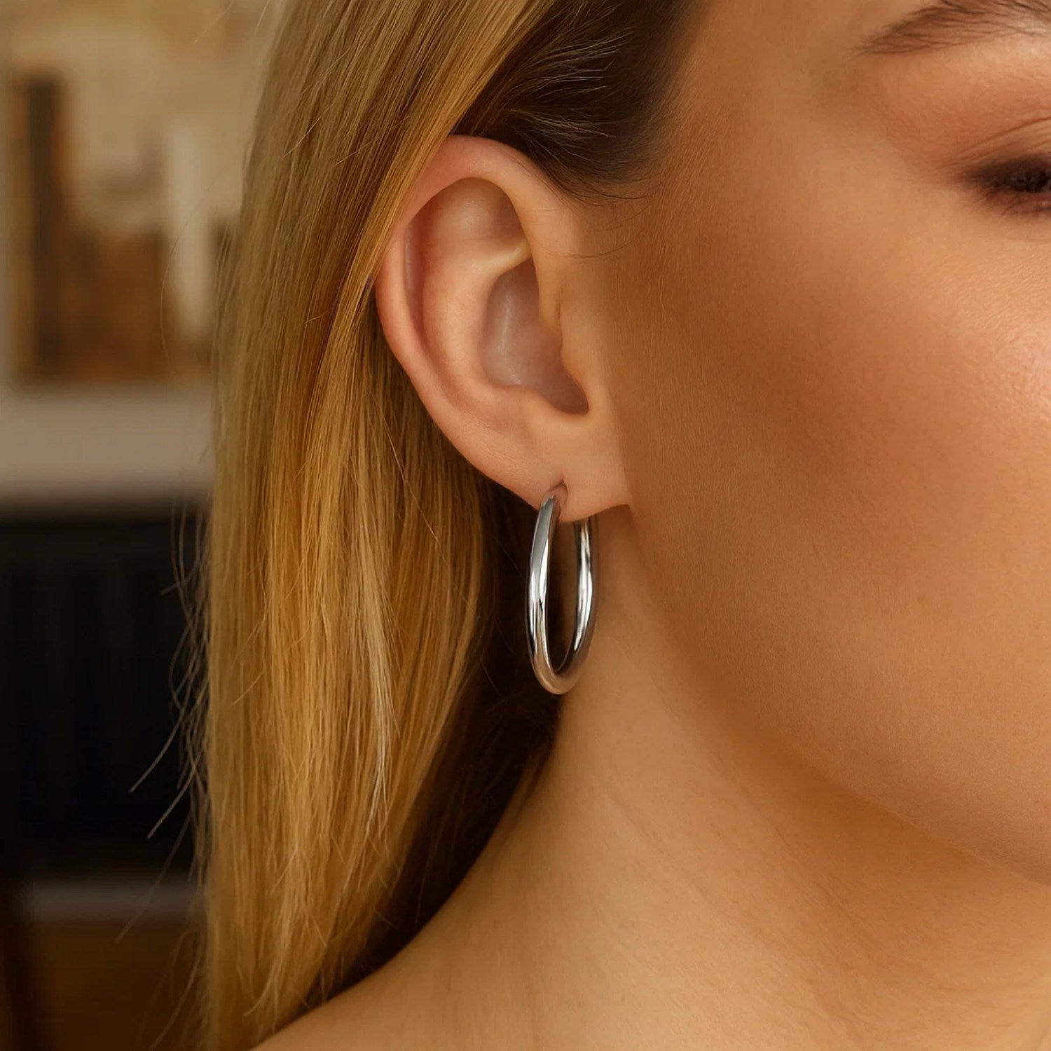 Sterling silver hoop earrings with polished rhodium plating on a woman's ear.