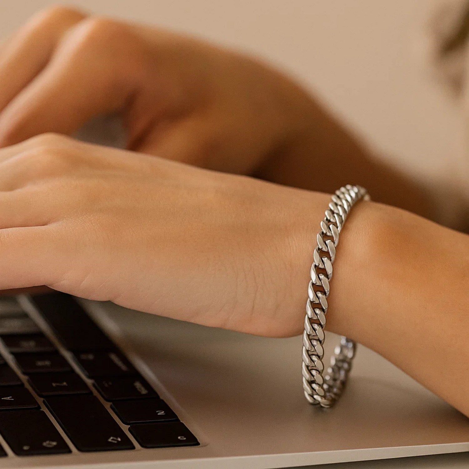 A person wearing a 14K white gold Cuban link bracelet while typing on a laptop.