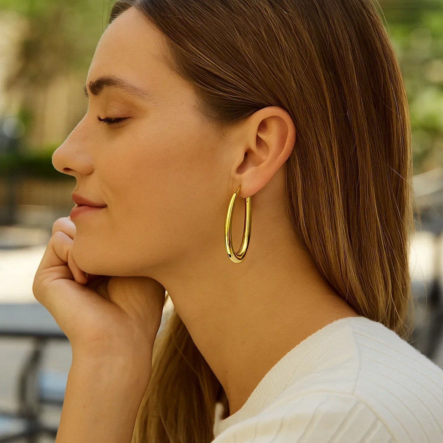 14k yellow gold elongated oval hoop earrings on a woman.