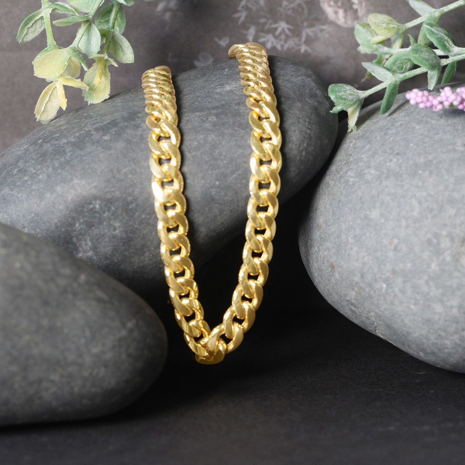 14k yellow gold Miami Cuban semi-solid chain draped over dark grey stones.