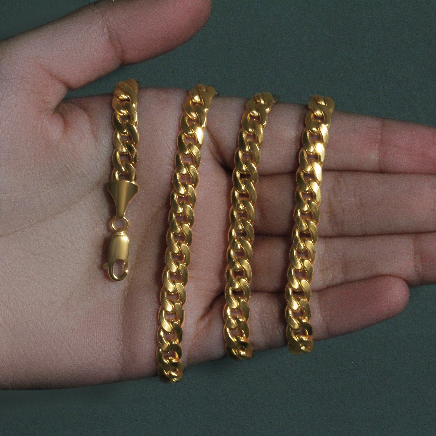 A 14k yellow gold Miami Cuban semi-solid chain with a lobster clasp is displayed on a hand.