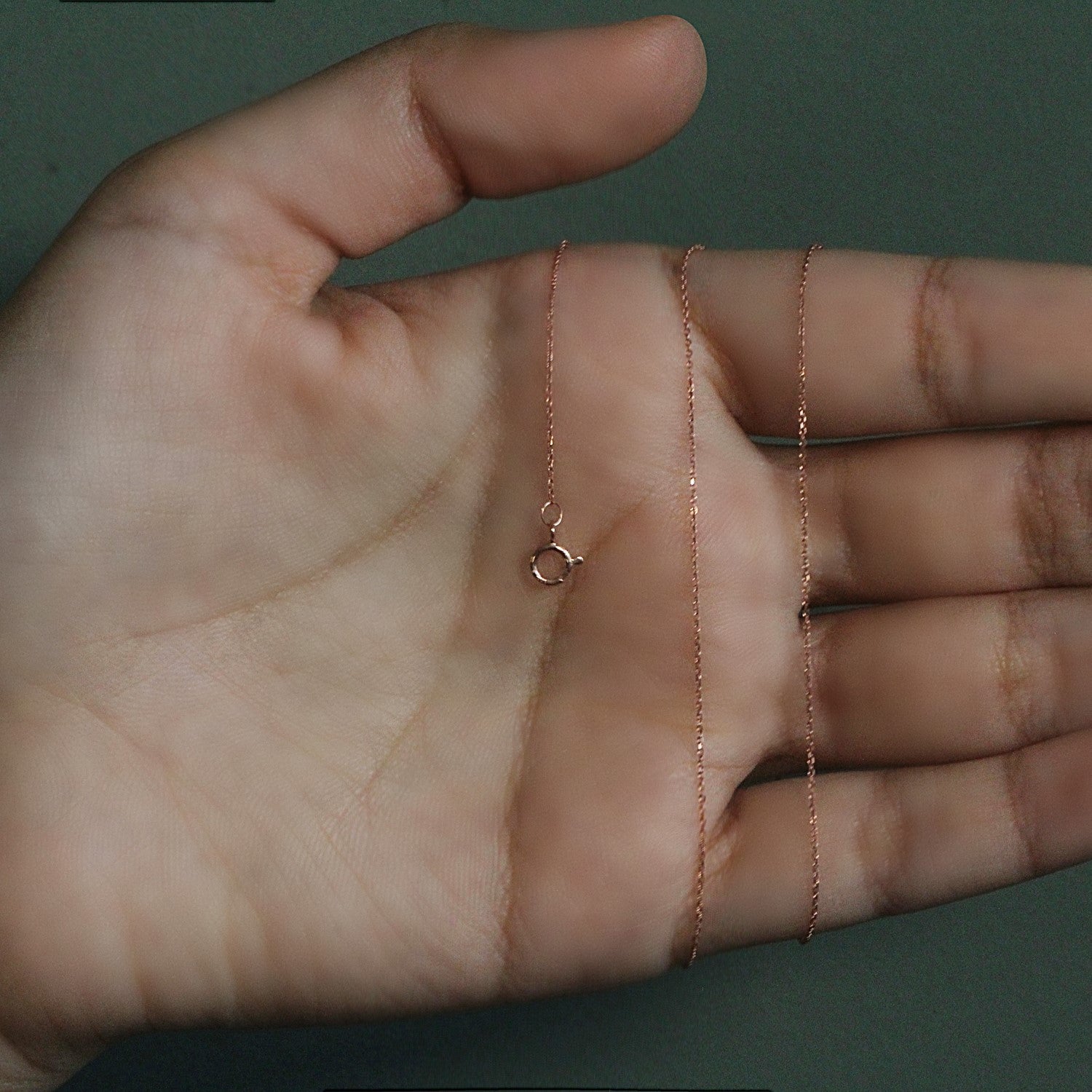 A 14k rose gold diamond cut cable link chain with a spring ring clasp held in a hand.