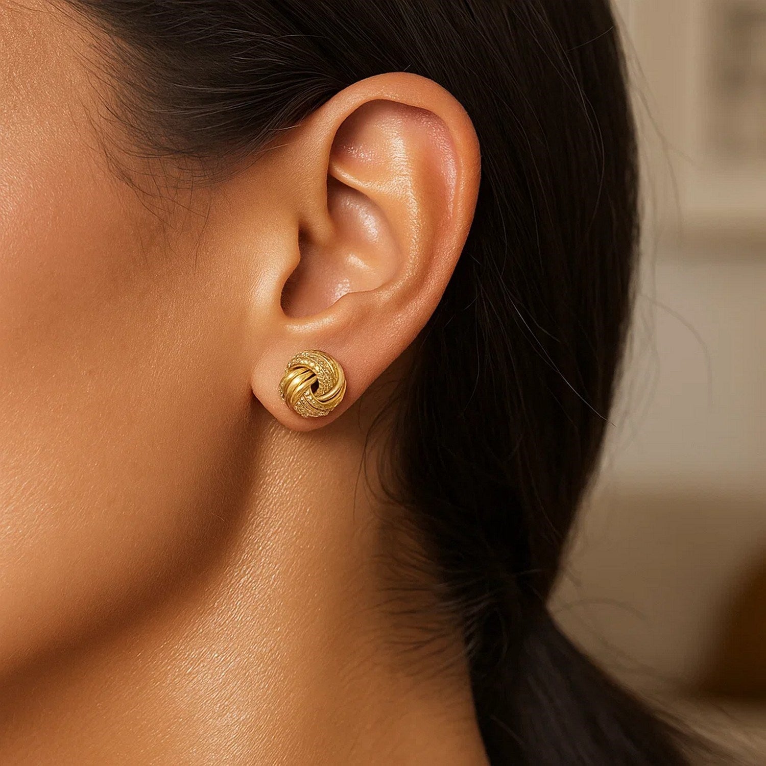 10k yellow gold love knot earrings with ridge texture on a person's ear.