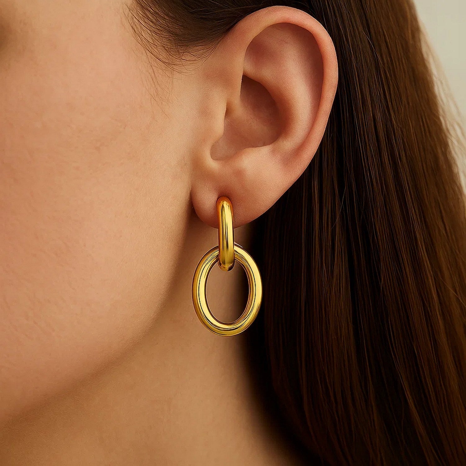 A close-up of a woman's ear wearing a pair of polished 14K yellow gold interlocking link drop earrings.
