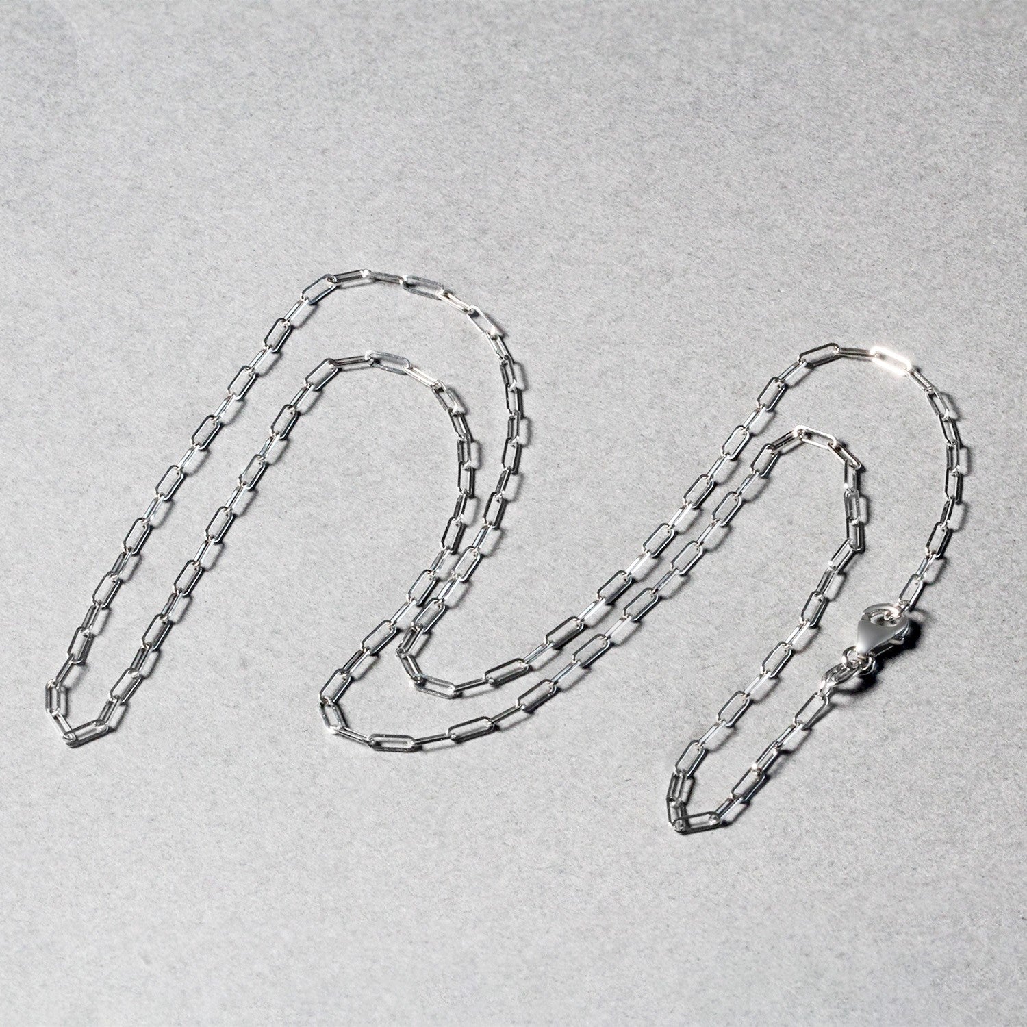 A 14K white gold paperclip chain with a lobster clasp is laid out on a gray surface.