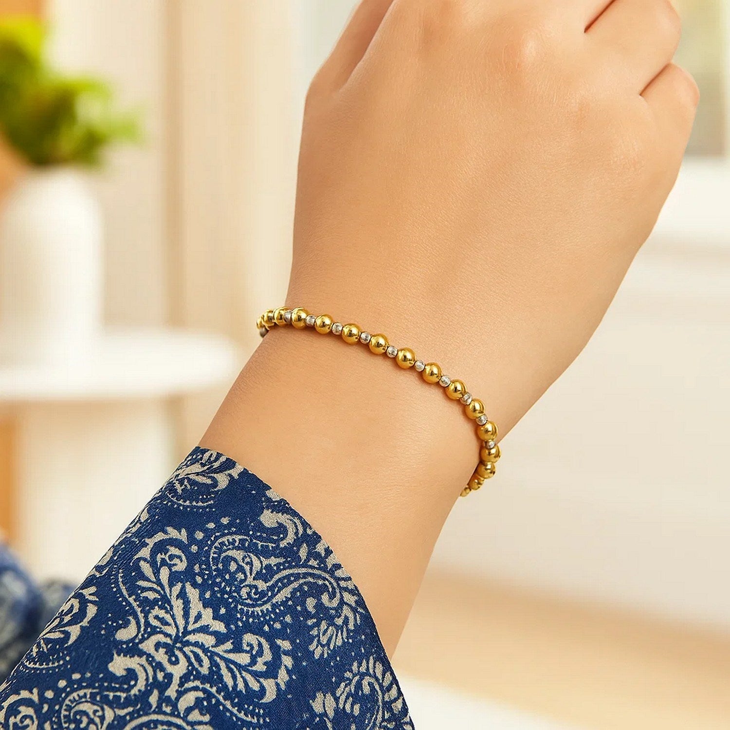 A two-tone gold bead bracelet with diamond-cut accents is worn on a wrist.