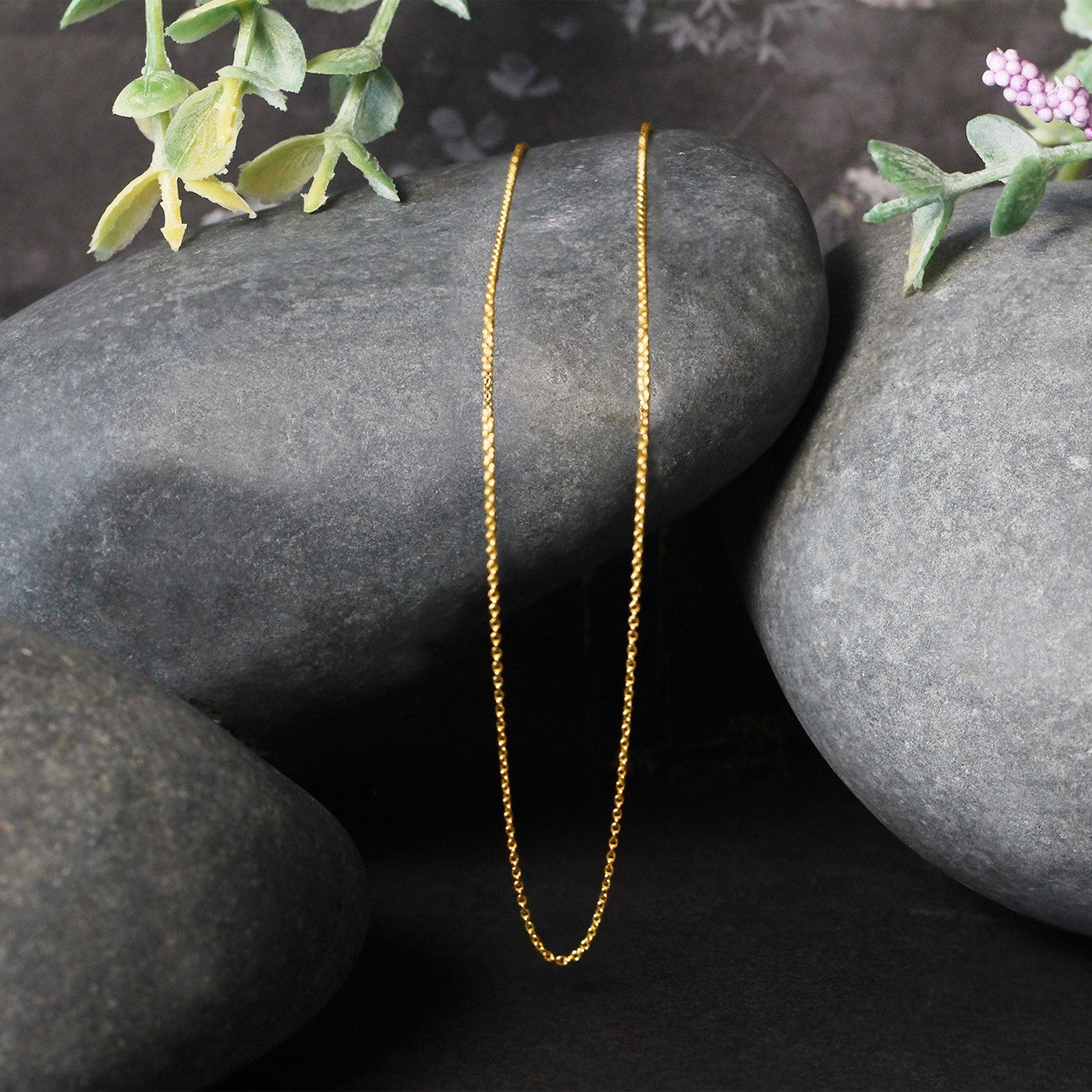 A delicate 14k yellow gold oval cable link chain rests on dark grey stones.