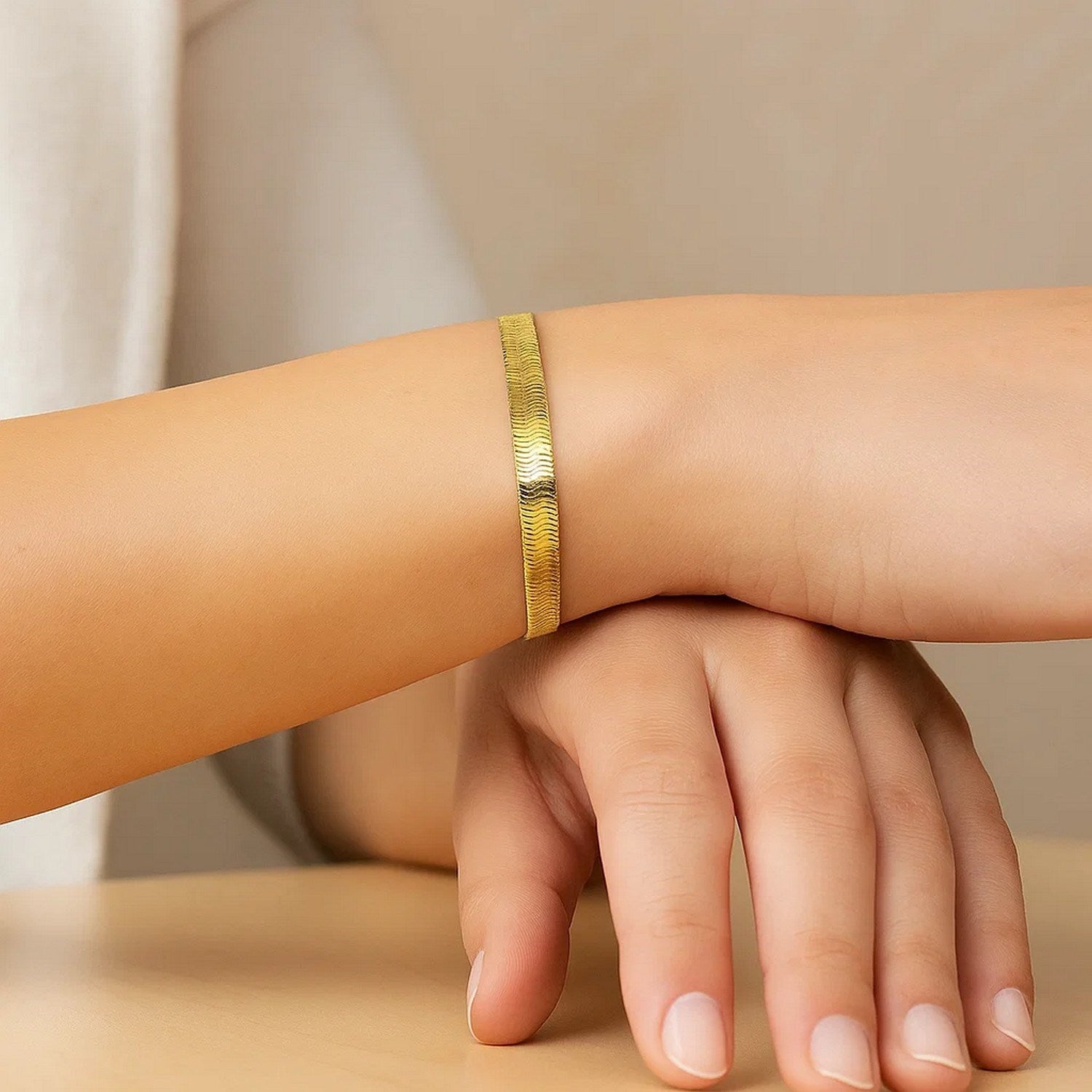A woman's arm and hand display a 10k yellow gold herringbone bracelet.