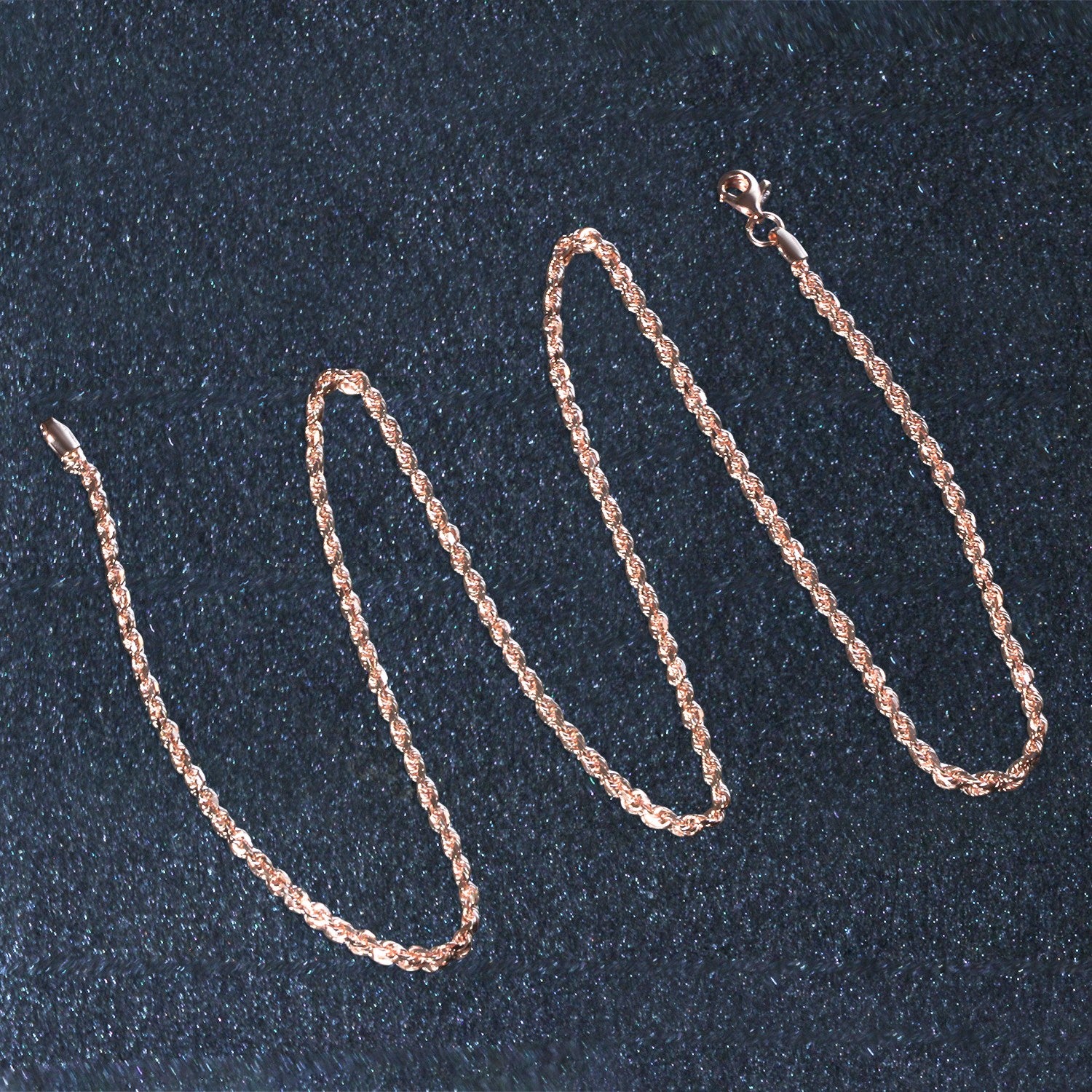 A rose gold diamond-cut rope chain with a lobster clasp is displayed on a dark surface.
