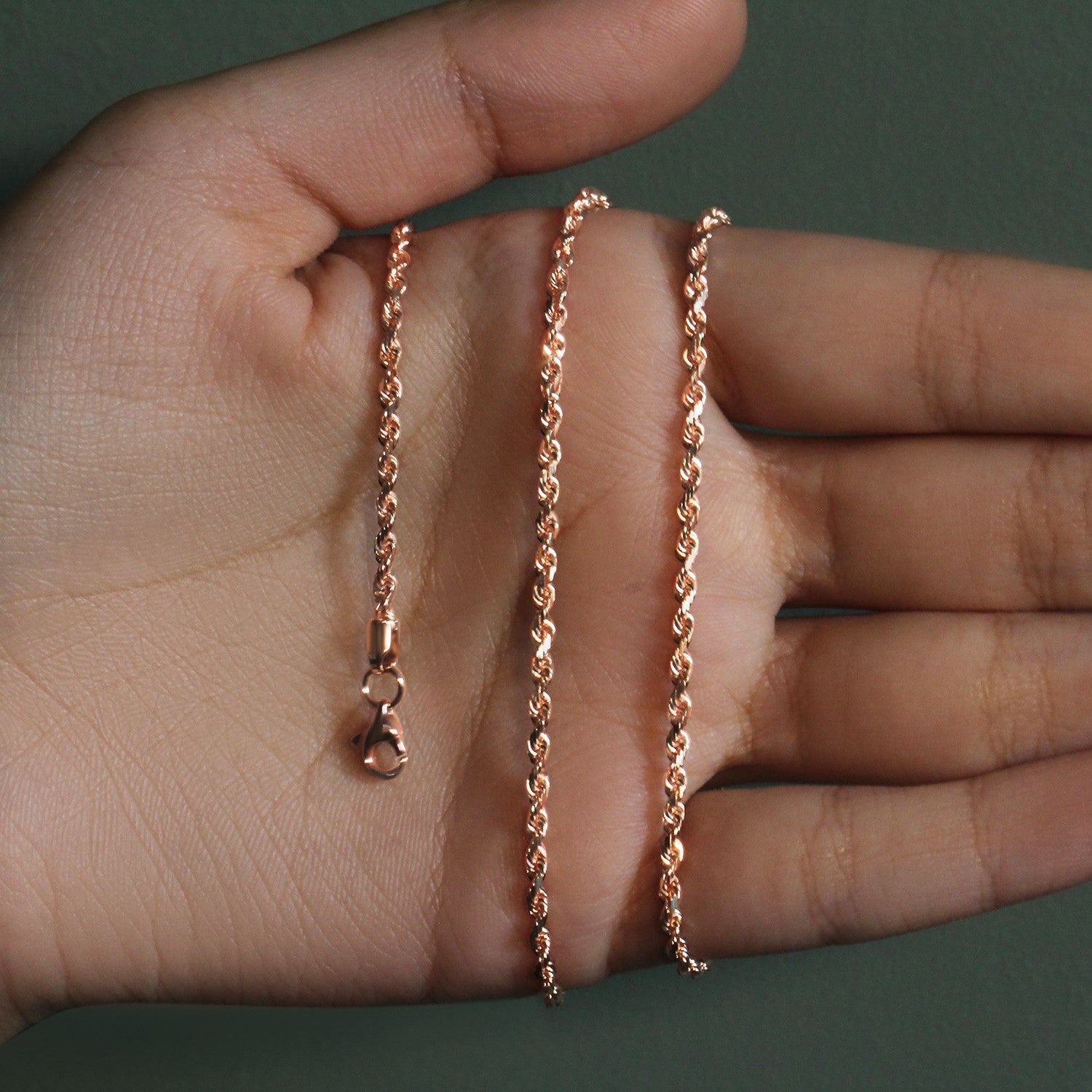 14k rose gold solid diamond cut rope chain with a lobster clasp on a hand.
