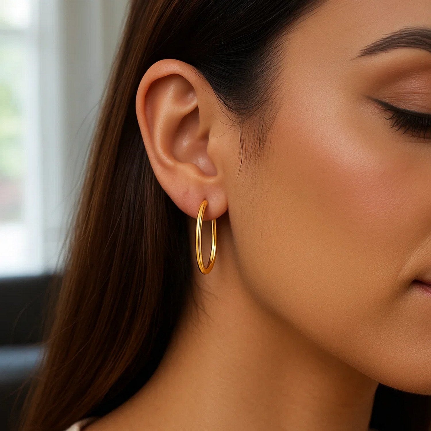 A woman wears a single 14k yellow gold endless oval hoop earring.