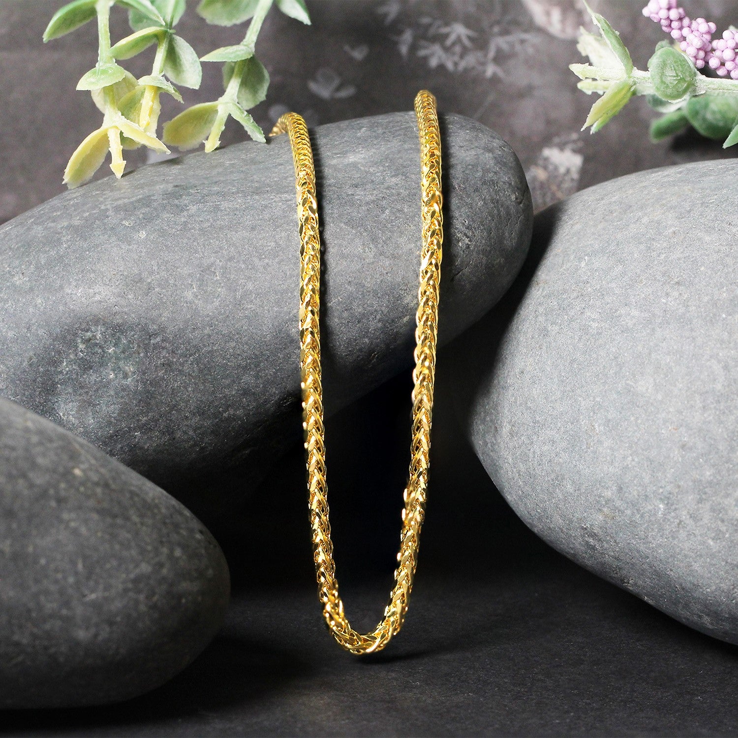 A 14k yellow gold diamond-cut round Franco chain is draped over dark gray rocks.