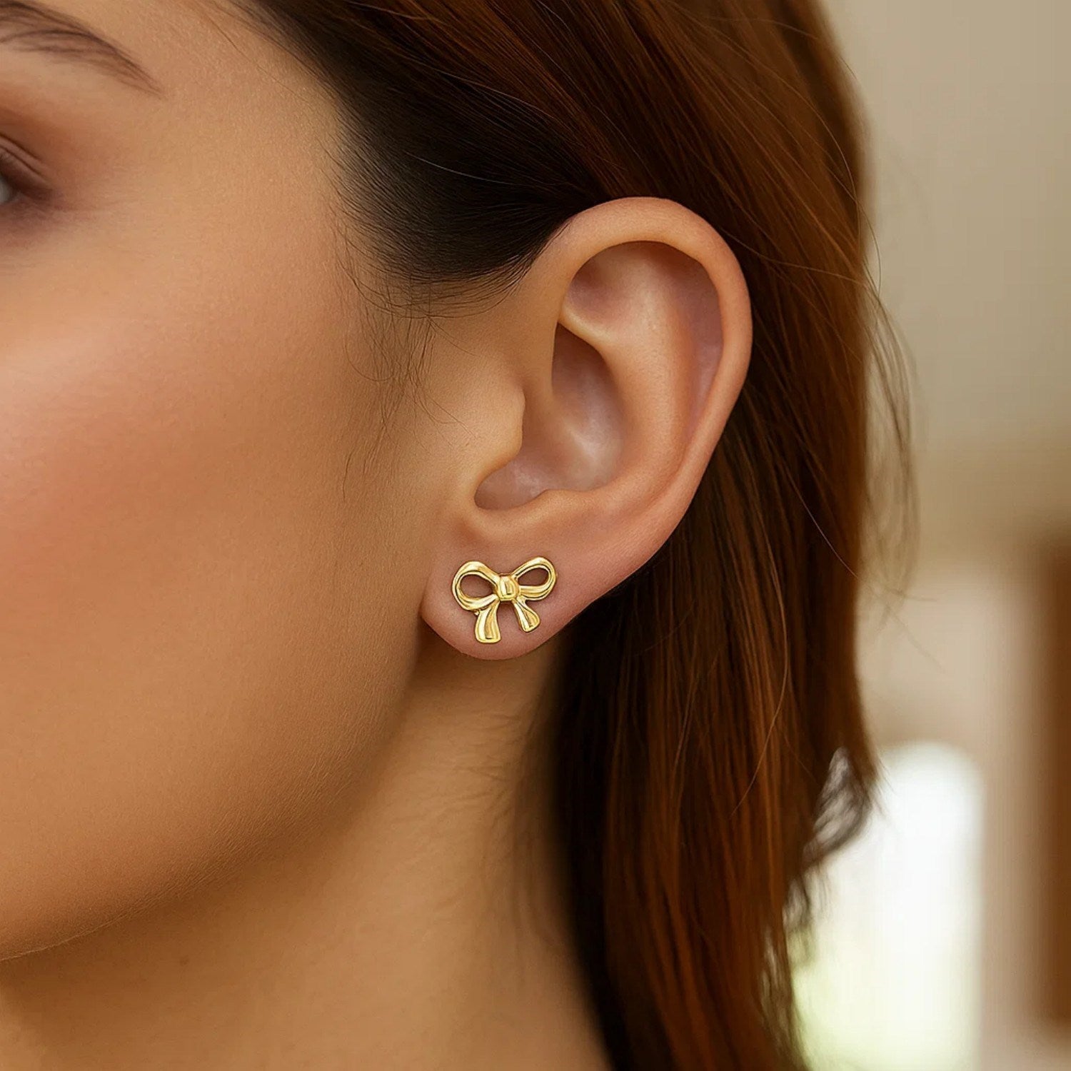14k yellow gold bow-style post earrings on a person's ear.