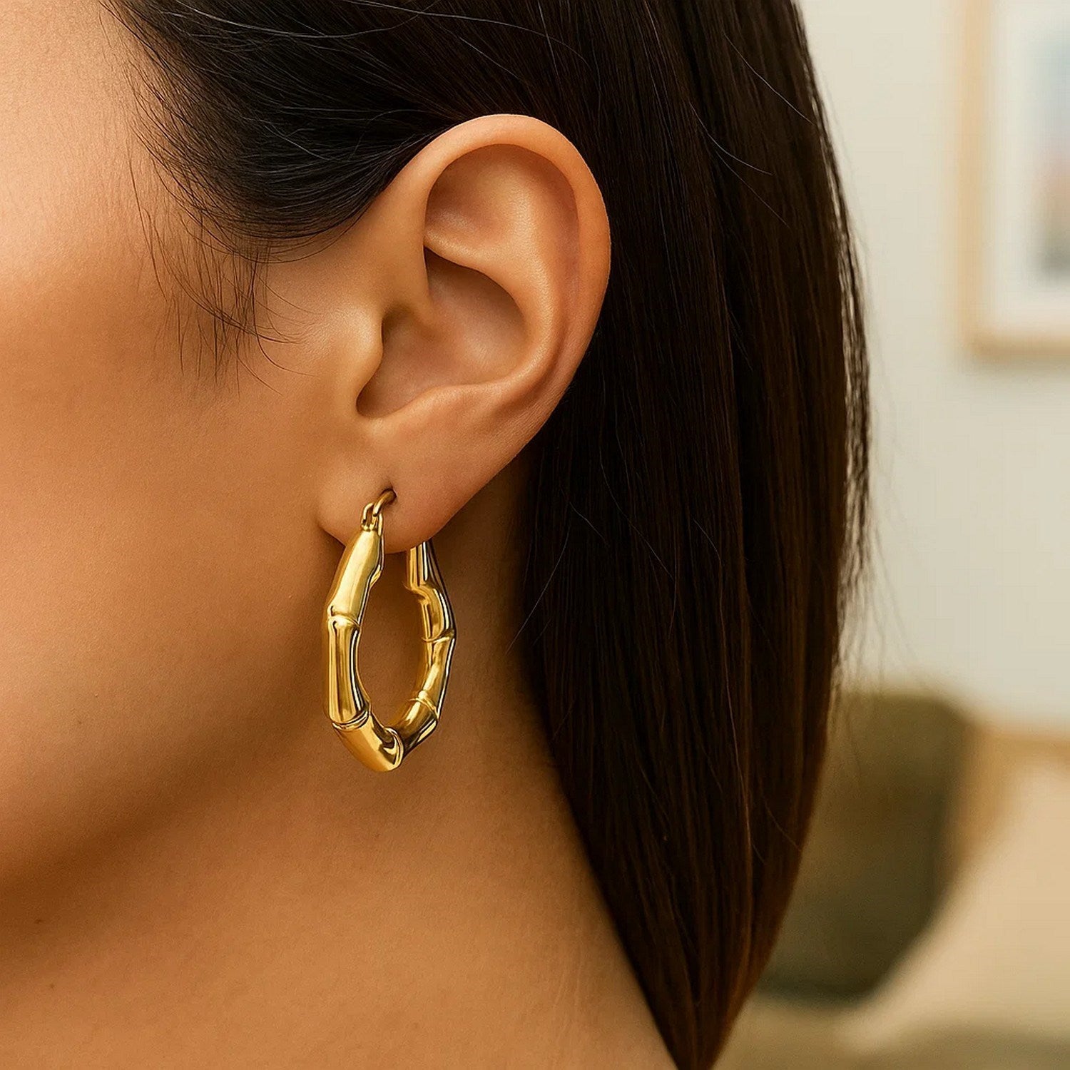 14k yellow gold medium bamboo hoop earrings on a woman's ear.