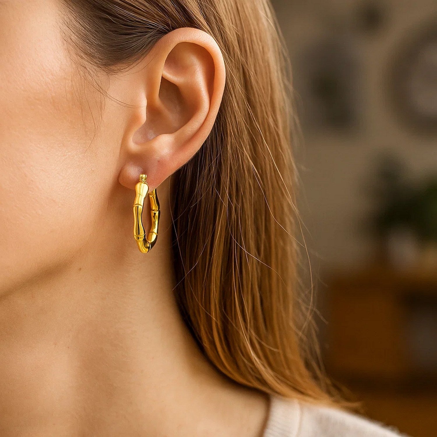 A woman wears a 14k yellow gold medium bamboo hoop earring.