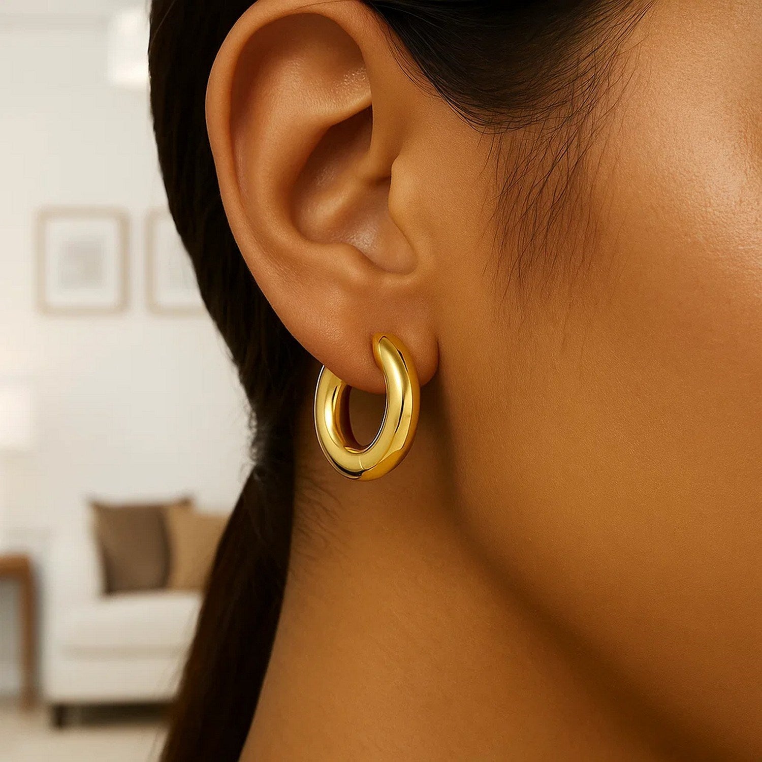 Large round electroform hoop earrings in 14K yellow gold on a person's ear.