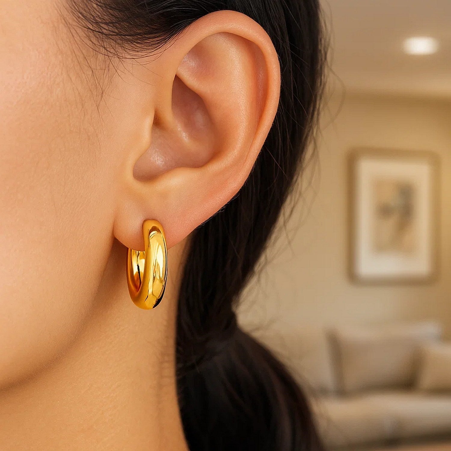 A woman wears a large, round, shiny 14K yellow gold hoop earring.