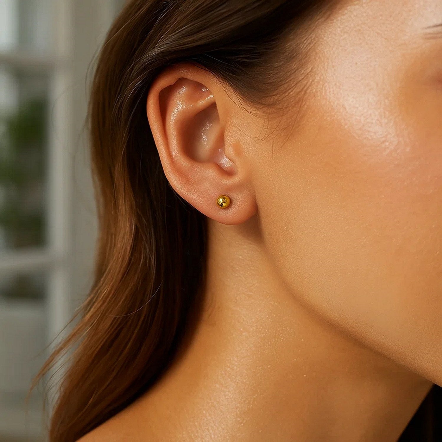 A single 10k yellow gold ball stud earring is worn on an ear.