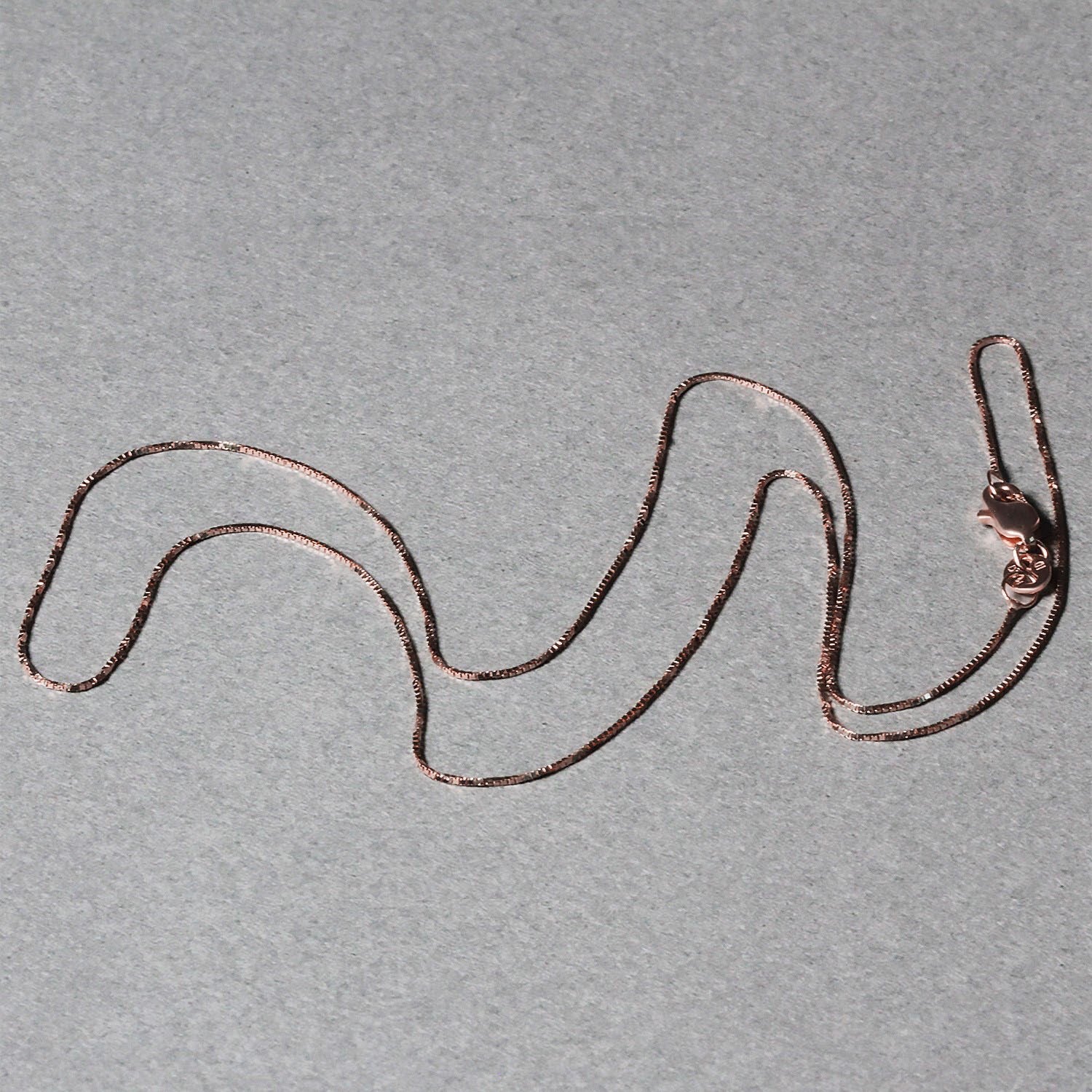 14k rose gold classic box chain with a lobster clasp on a gray background.