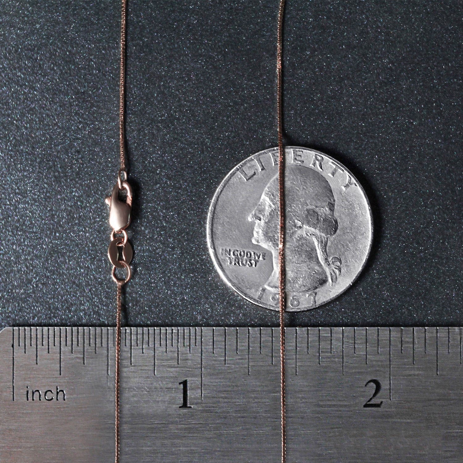 A 14k rose gold classic box chain with a lobster clasp, measured against a ruler and coin.
